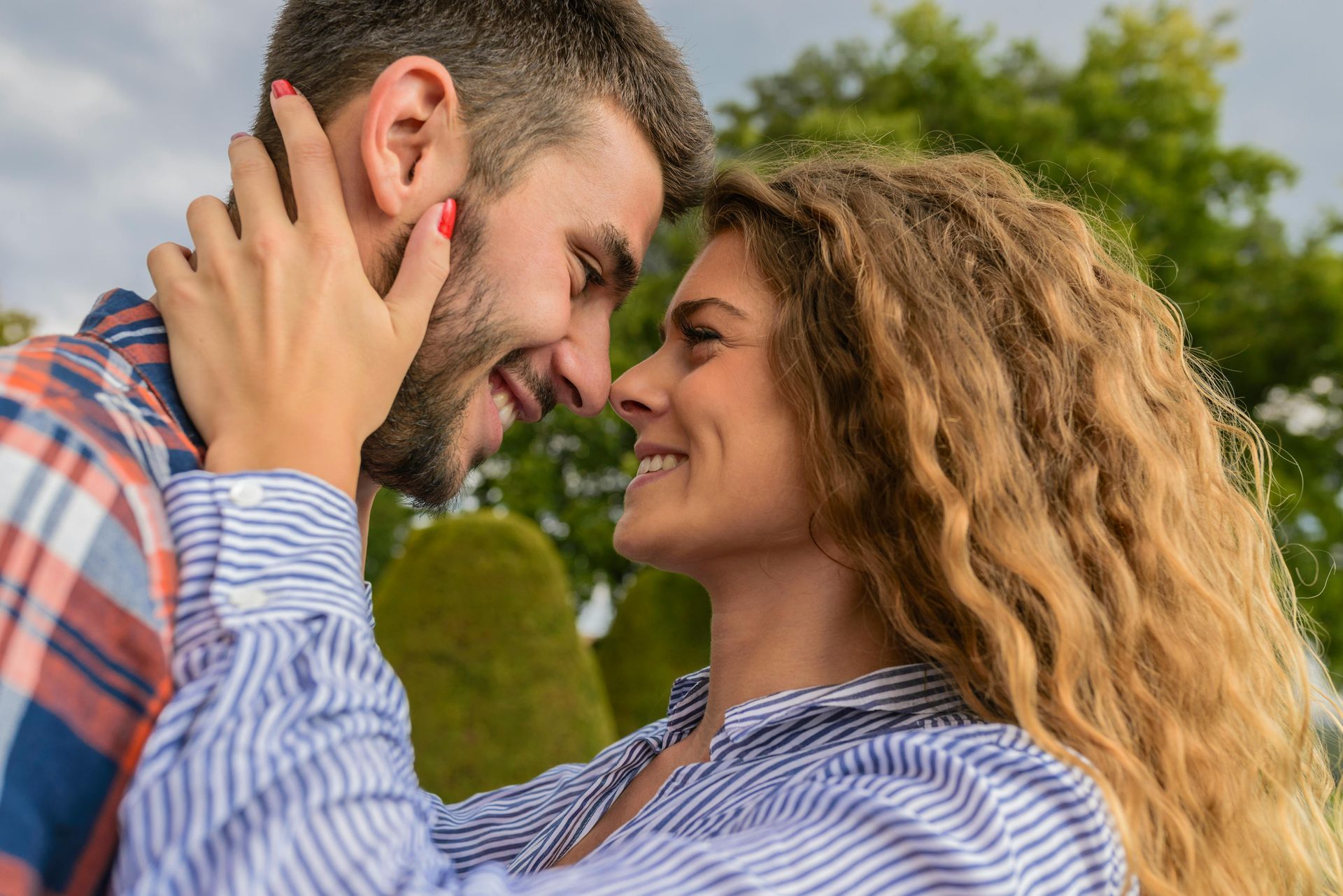 Woman tenderly touches a man's face as they look at each other with smiles, outdoors.