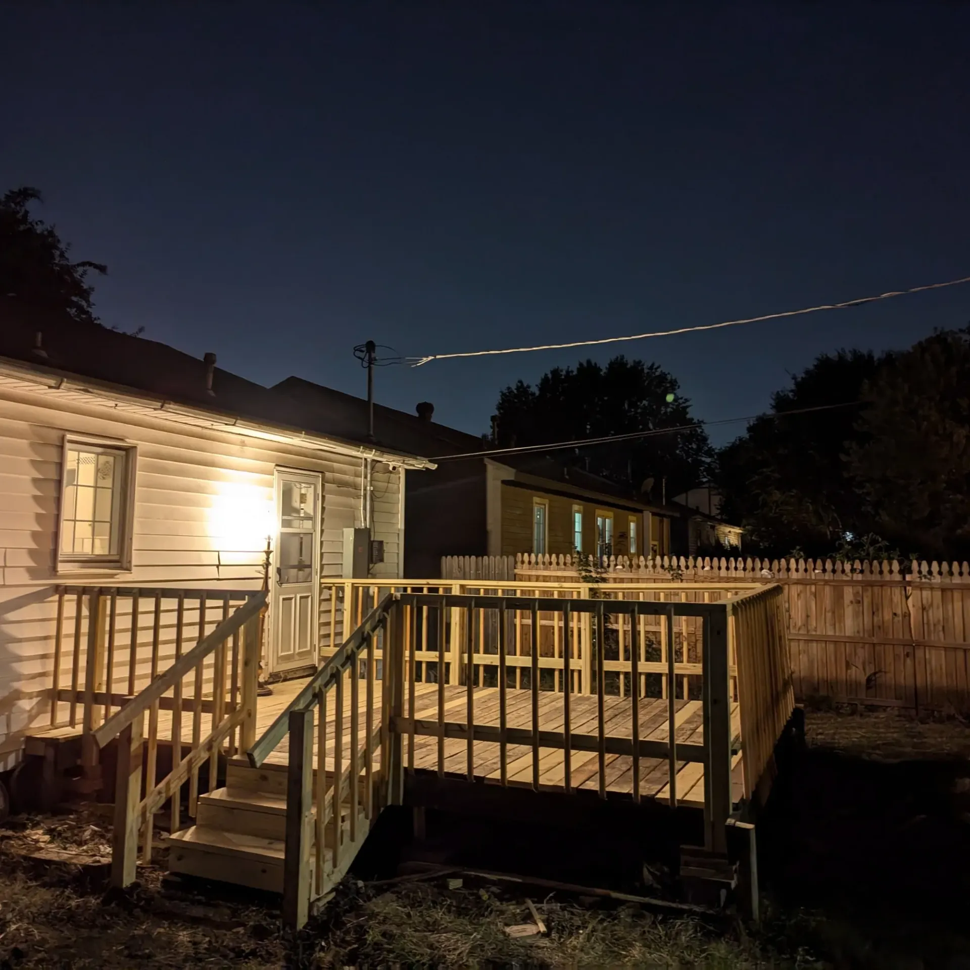 Aarons Repair and Remodel - A house with a wooden deck and stairs at night