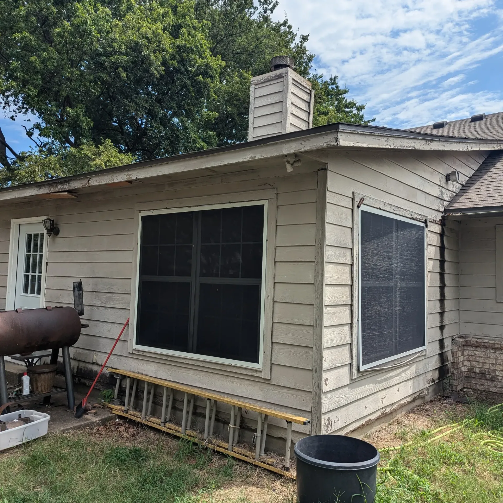 Aarons Repair and Remodel - A white house with a ladder and a grill in the backyard.