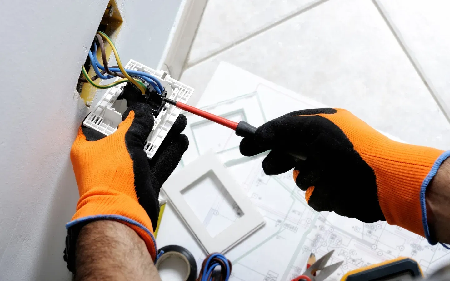 An electrician is working on a light switch with a screwdriver.