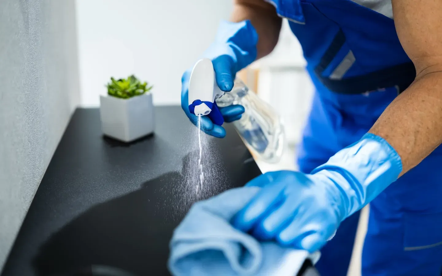 A man wearing blue gloves is cleaning a sink with a cloth.