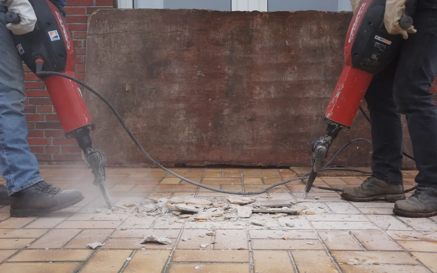 Two men are using hammers to break bricks on a sidewalk.