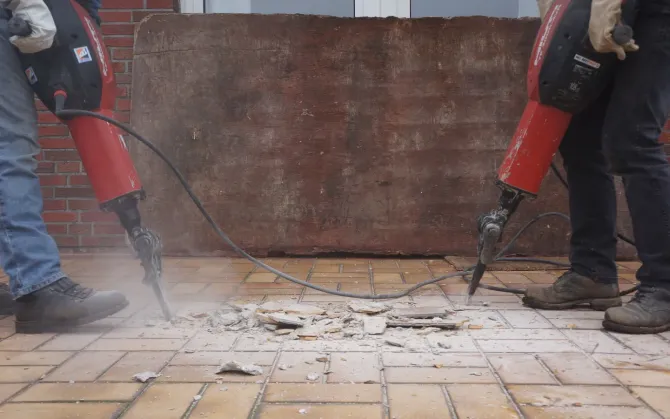 Aarons Repair and Remodel - Two men are using hammers to break bricks on a sidewalk.