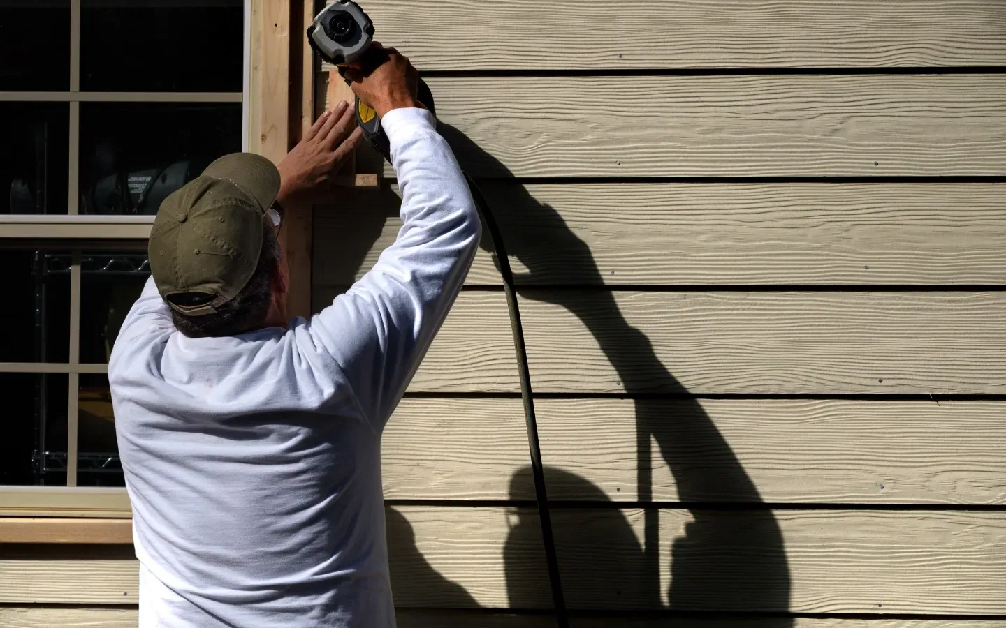 Aarons Remodel and Repair - A man is using a drill to fix a window on a house.