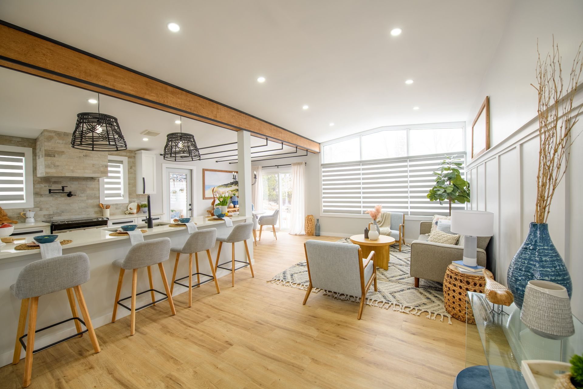 Open-concept living space with kitchen and living room. Light wood floors, white walls, and gray furniture.