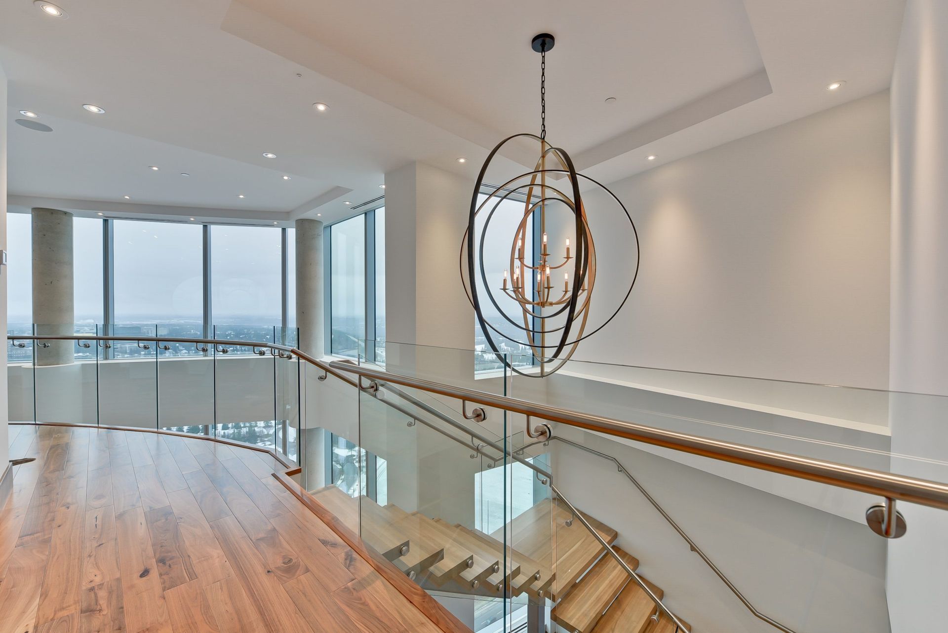 Modern apartment interior with a staircase, glass railings, and a large chandelier.