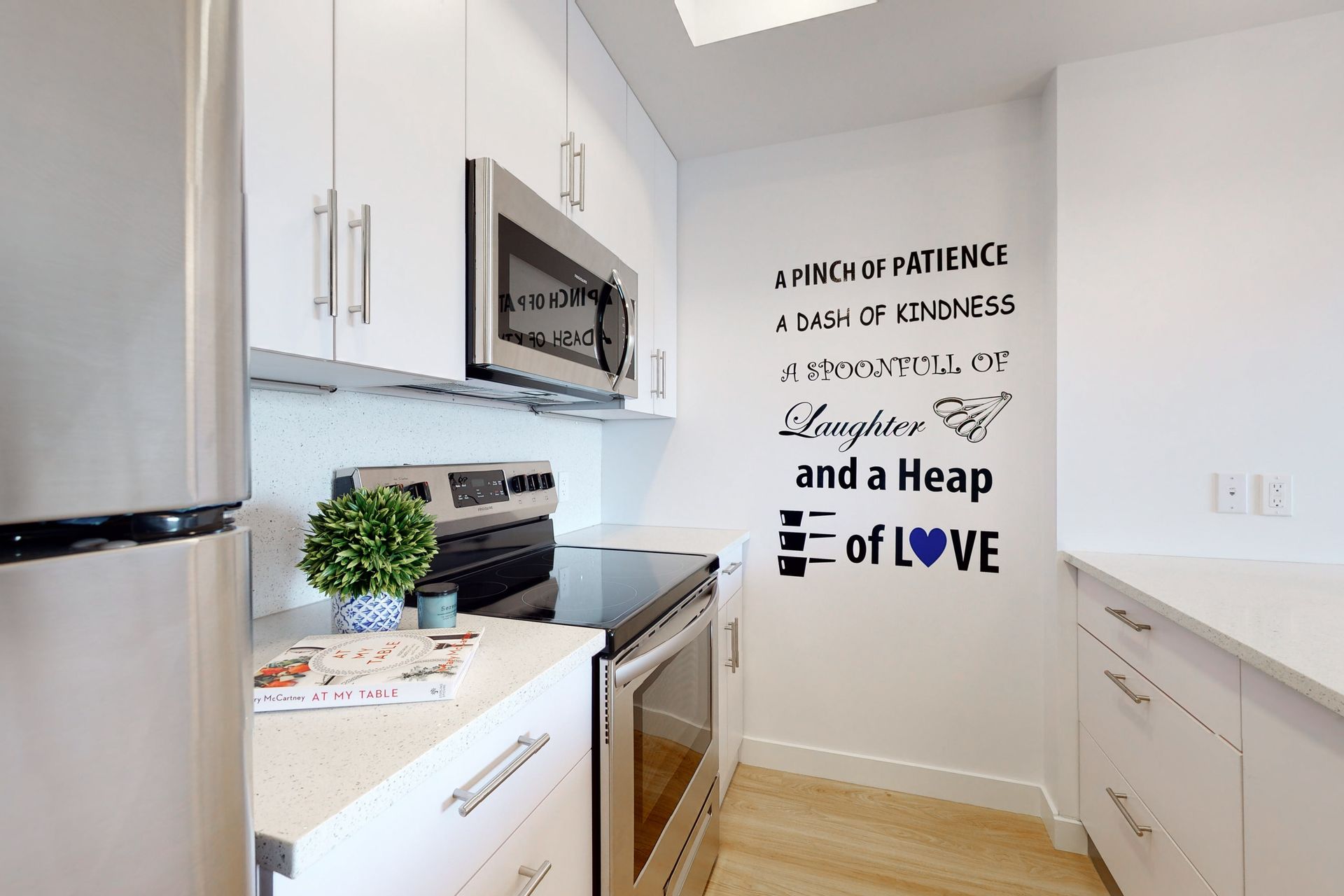 A kitchen with white cabinets and stainless steel appliances and a wall decal that says daughter and a heap of love.