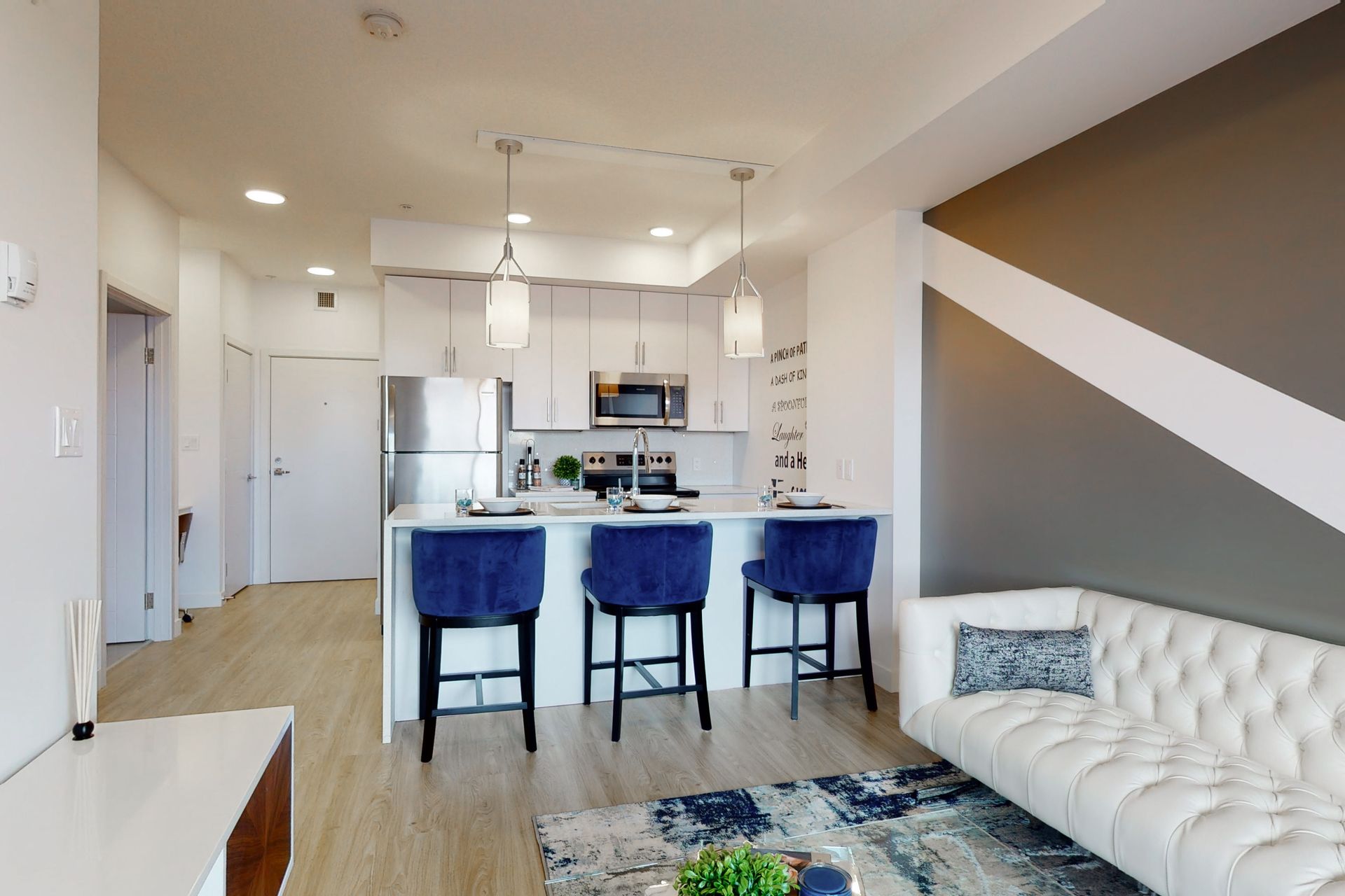 A living room with a couch , stools , and a kitchen.