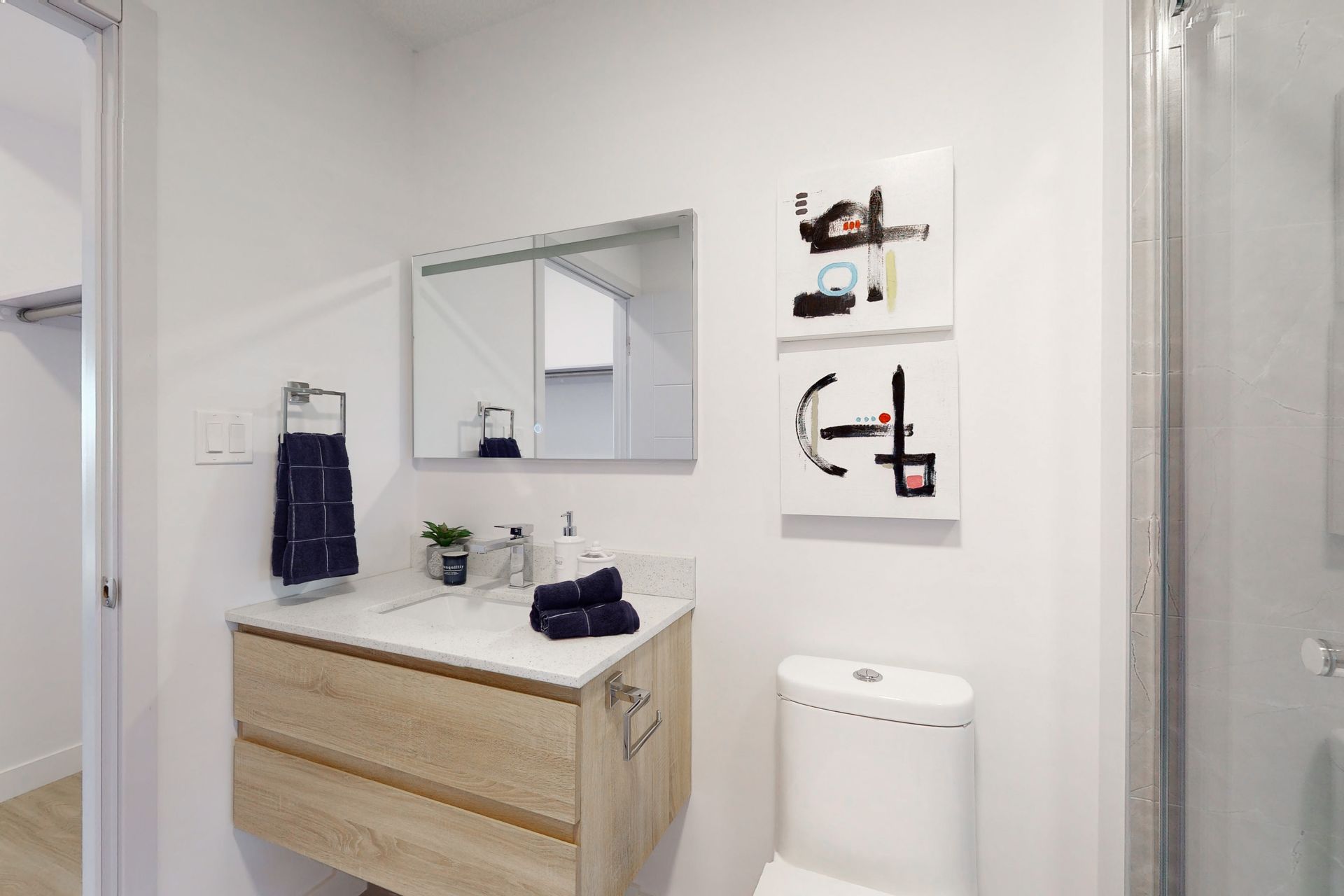 A bathroom with a sink , toilet , mirror and paintings on the wall.