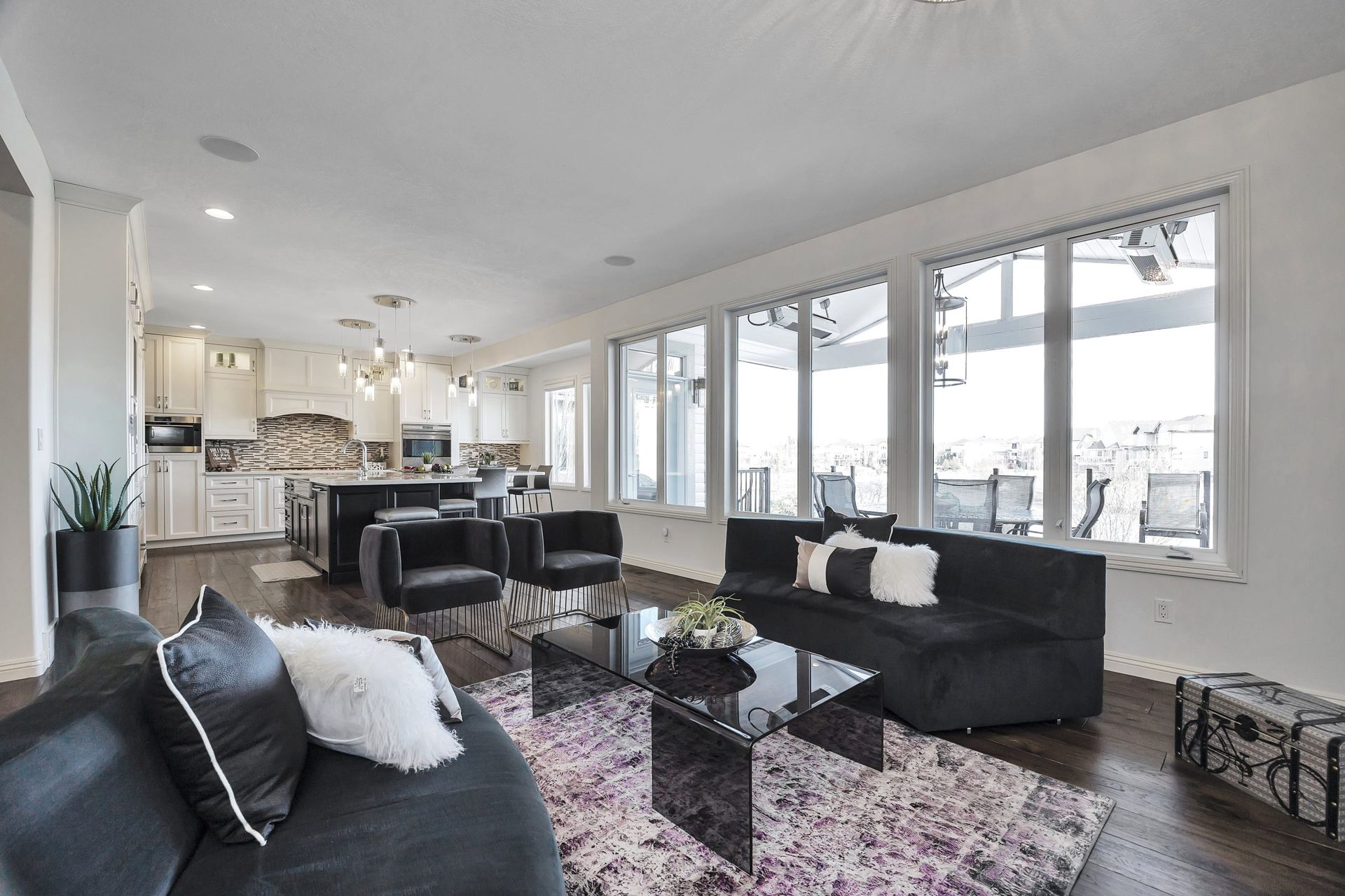 Spacious modern living room with black couches, dark wood floors, and large windows.