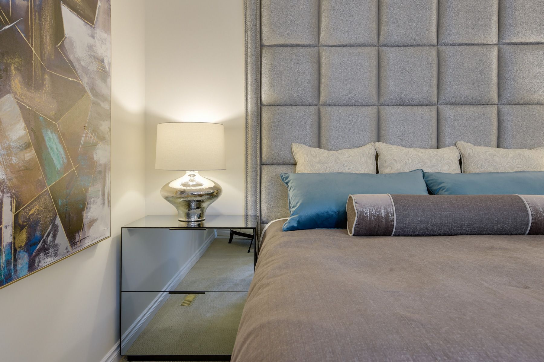 A bedroom with a bed , nightstand , lamp and painting on the wall