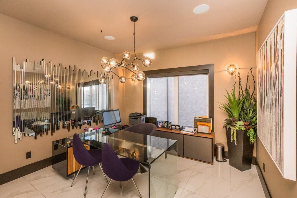 A room with a desk , chairs , a chandelier and a painting on the wall.