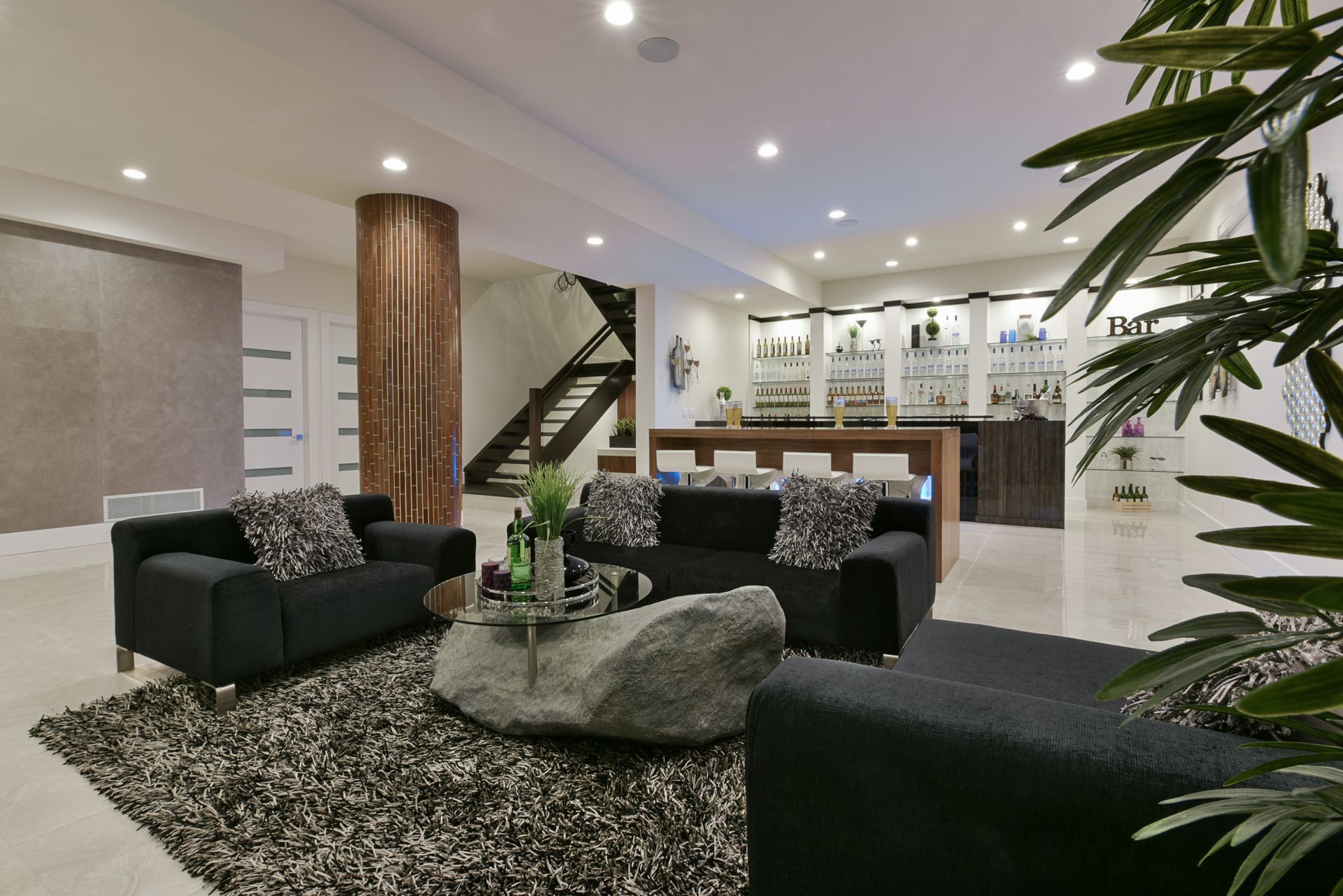 A modern basement lounge with black sofas, a rock coffee table, and a bar.