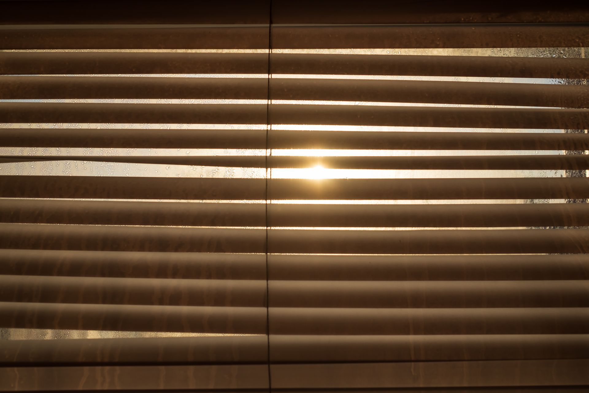 The sun is shining through the blinds of a window.