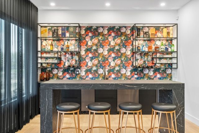 A kitchen with a bar and stools and a floral wallpaper on the wall.