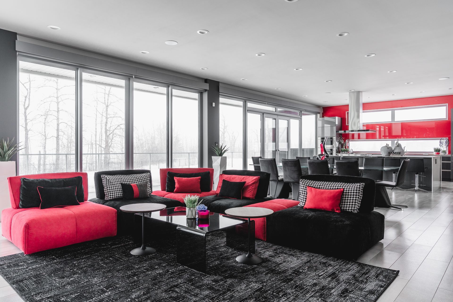 Modern living room with red and black furniture, large windows, and a black rug.