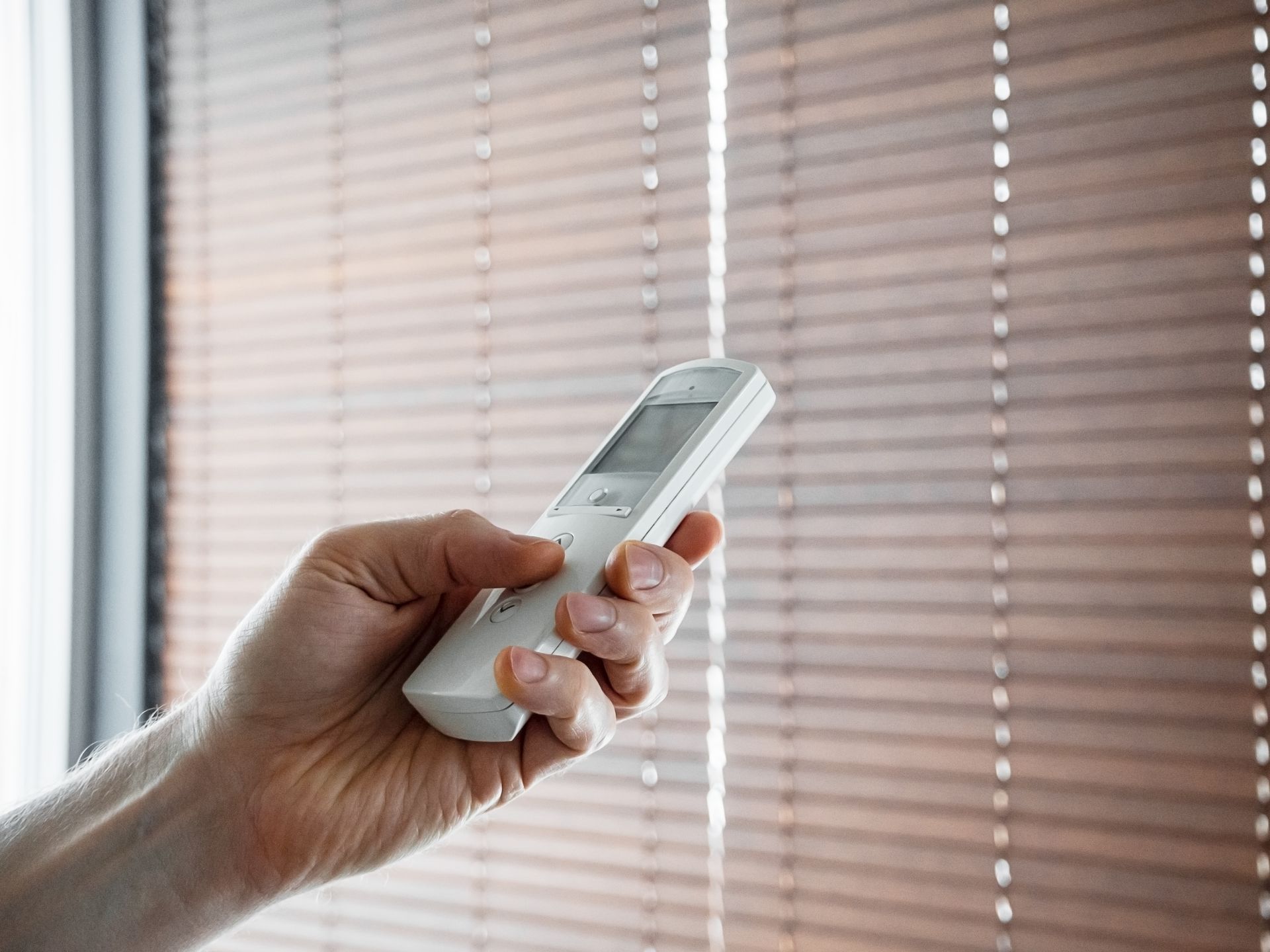 A person is using a remote control to control blinds.
