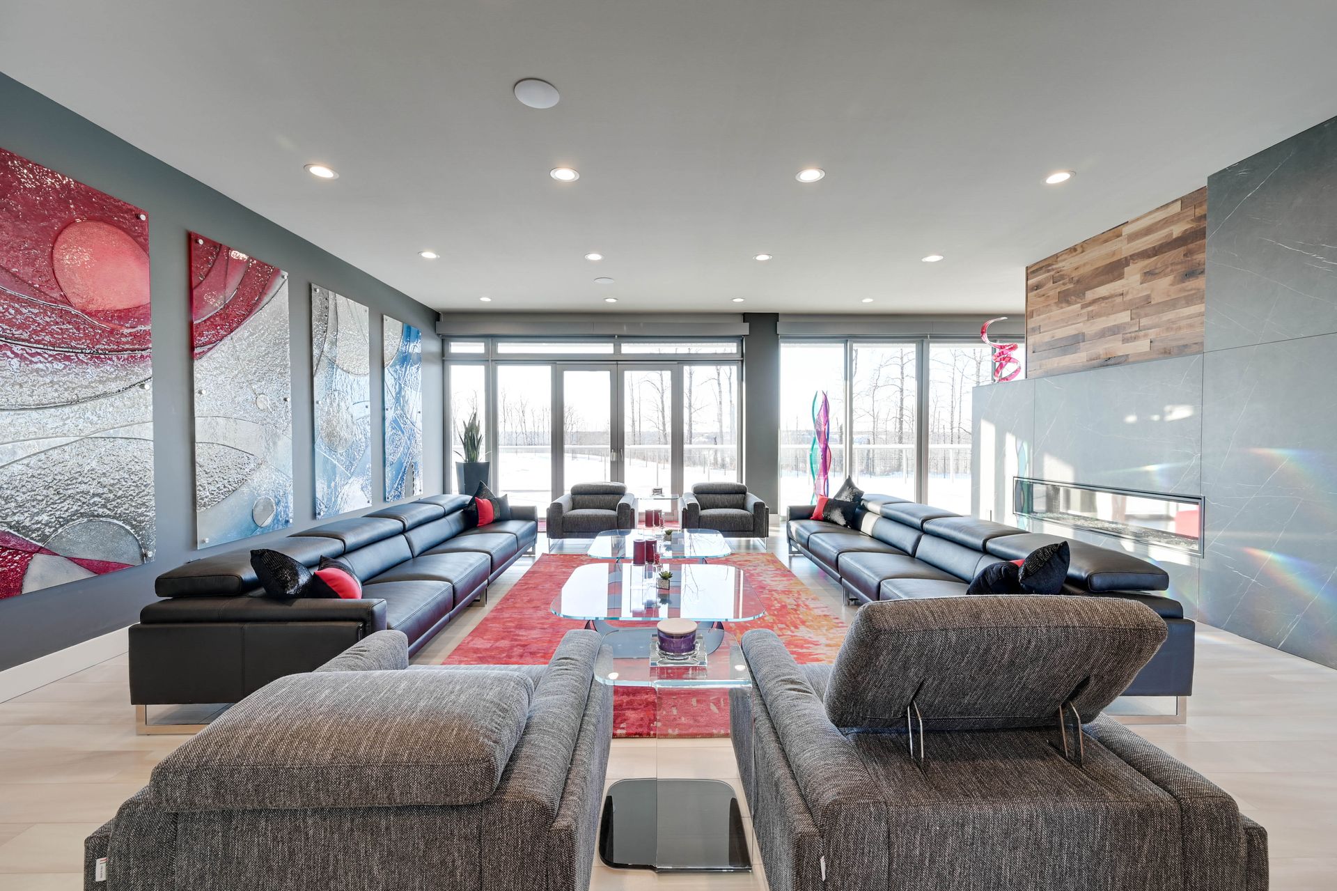 Modern living room with long black sofas, red rug, and artwork.