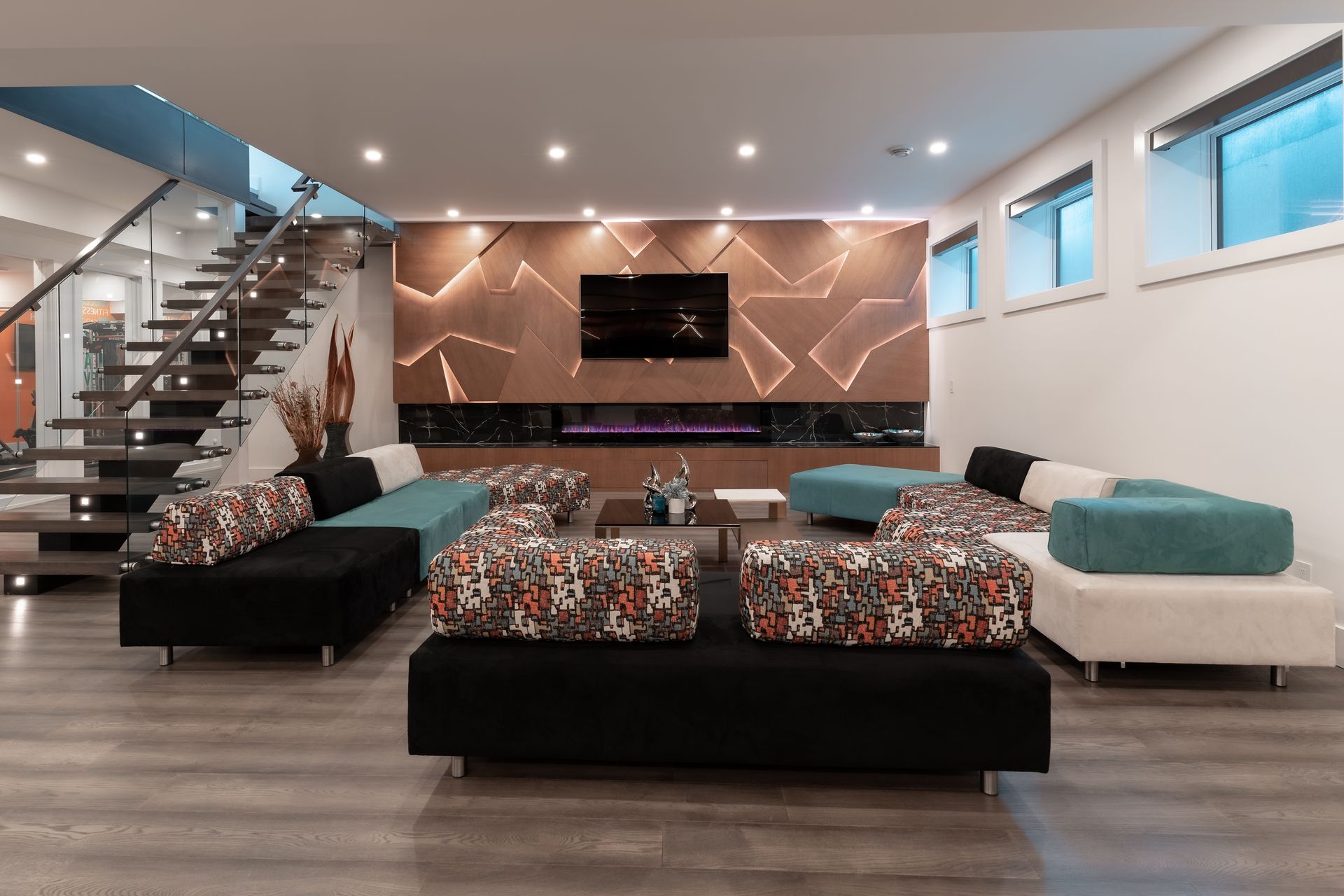 Modern basement living room with sofa seating, fireplace, TV, and stairs.