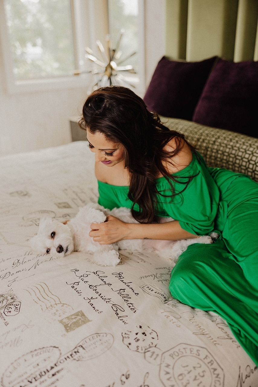 A woman in a green dress is laying on a bed with a white dog.
