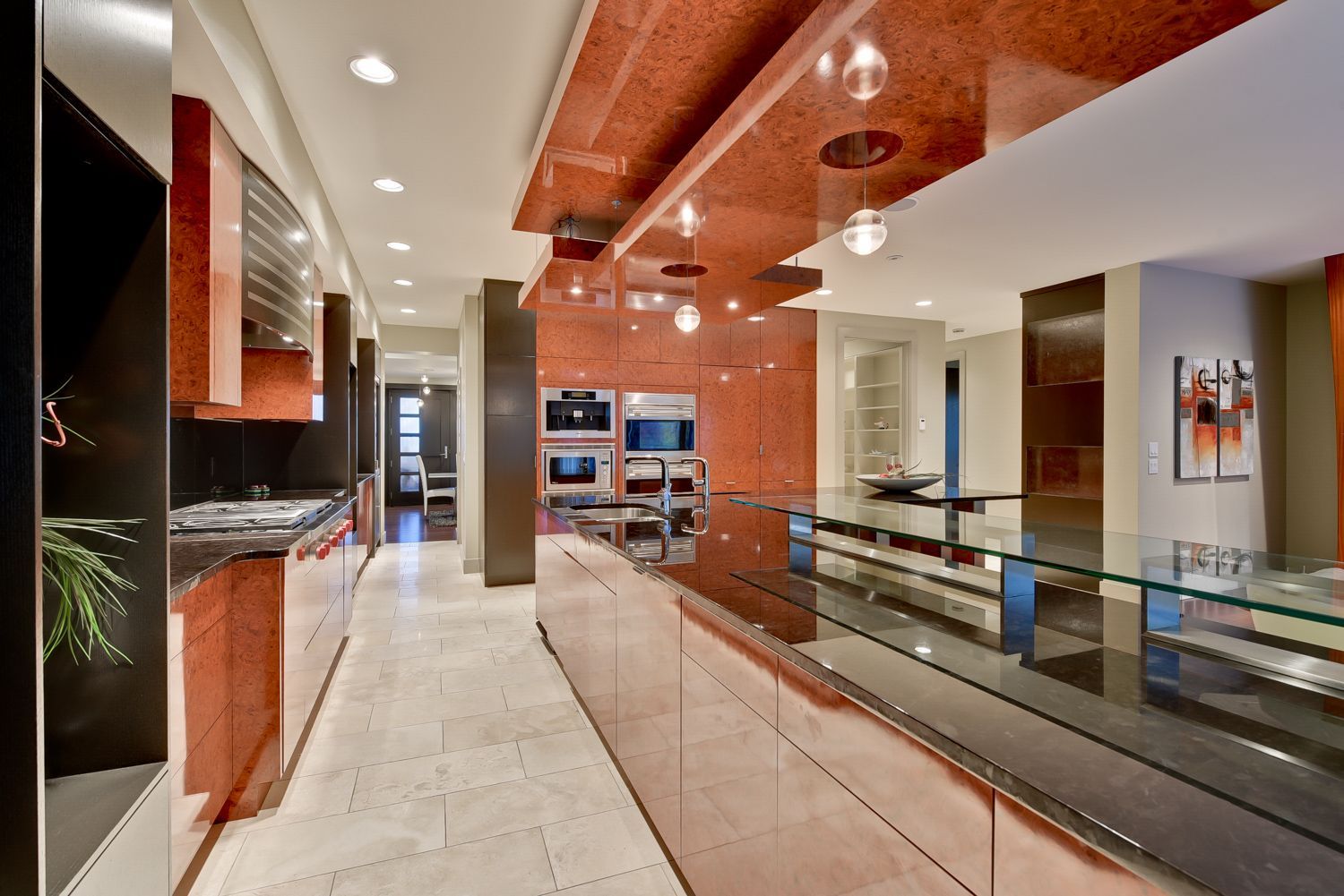 Modern kitchen with red granite ceiling and counters, stainless steel appliances, and a long glass-topped island.