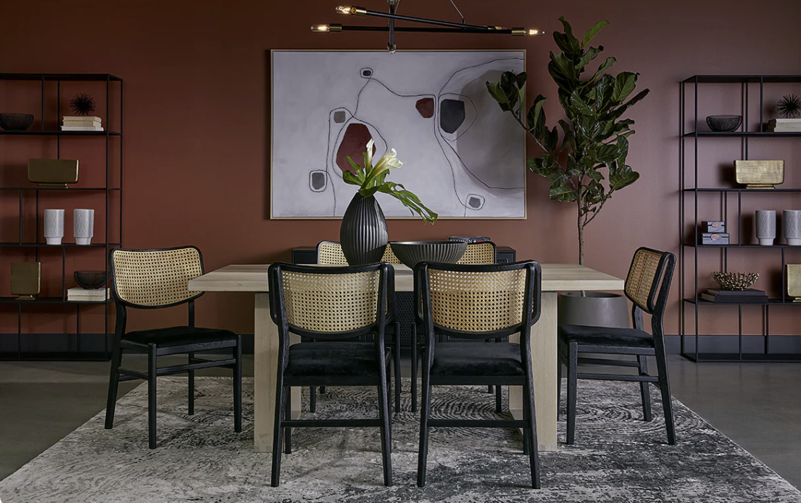 A dining room with a table and chairs and a painting on the wall.