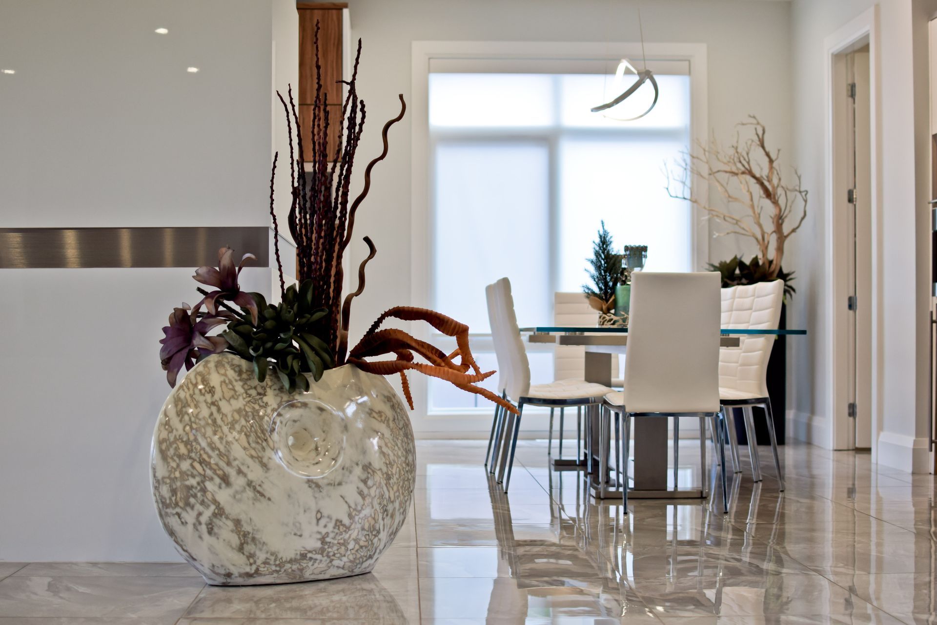 A dining room with a table and chairs and a large vase with flowers in it
