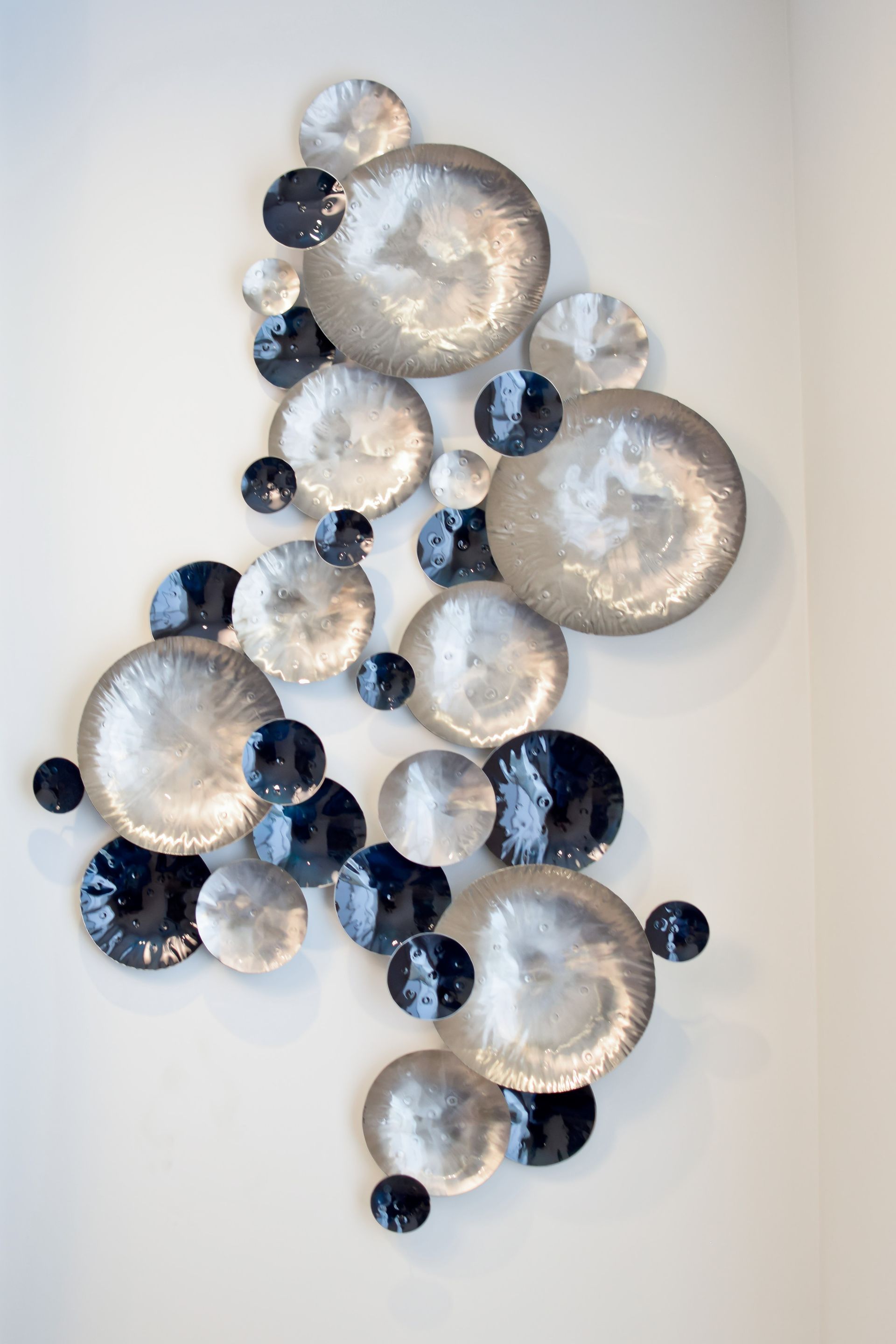 A group of silver and black plates are hanging on a white wall.