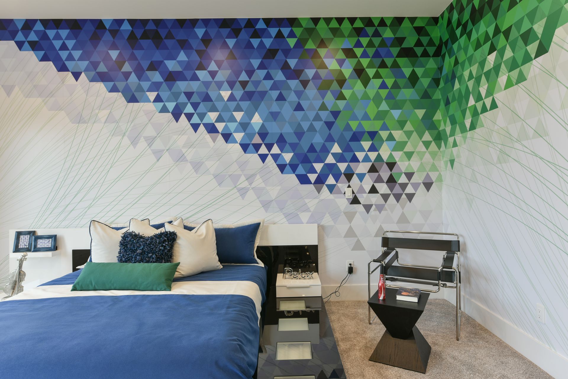 A bedroom with a bed a chair and a wall with triangles painted on it