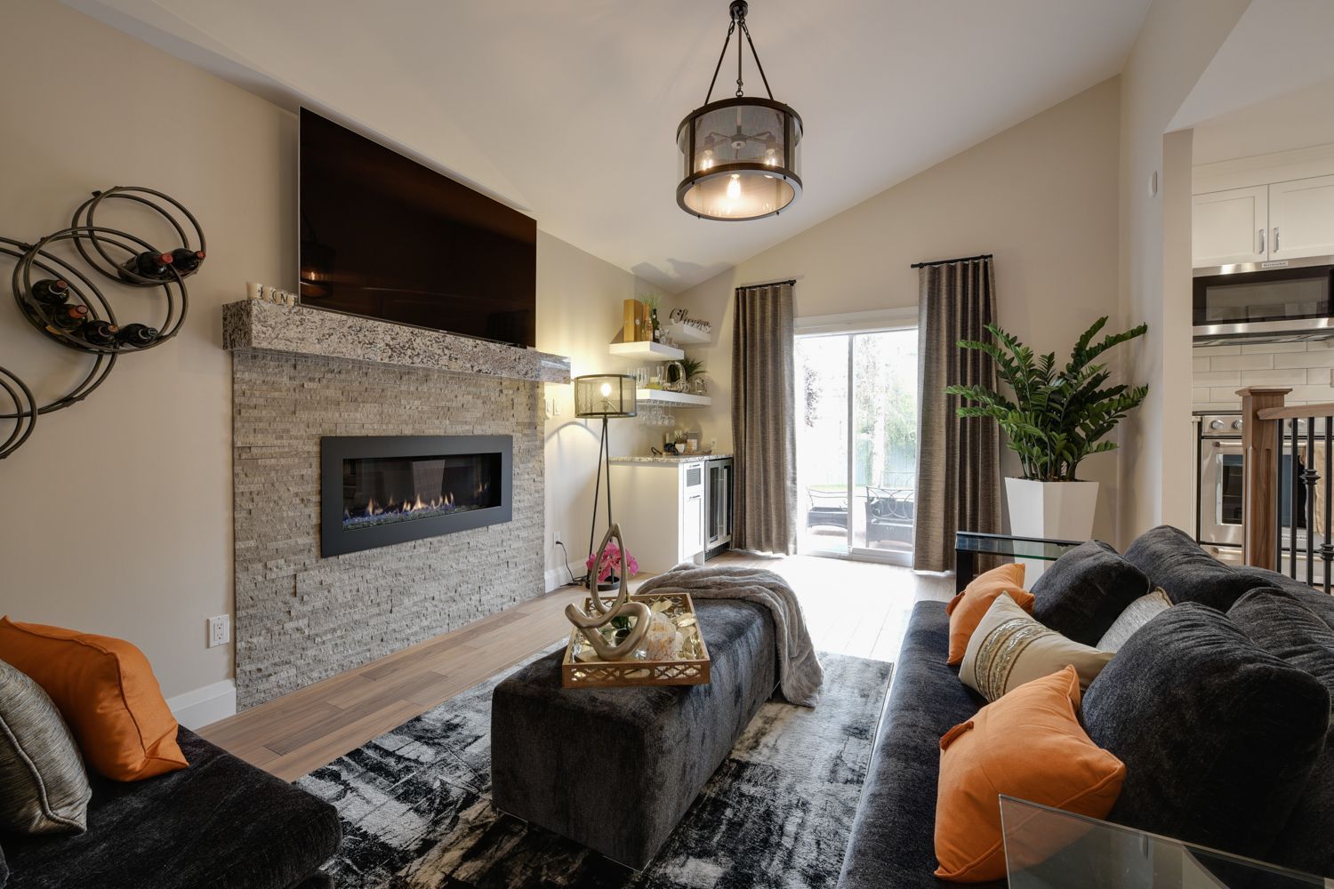 Living room with fireplace, TV, and a black sectional sofa with orange and grey pillows. Sliding glass door leads to outdoors.