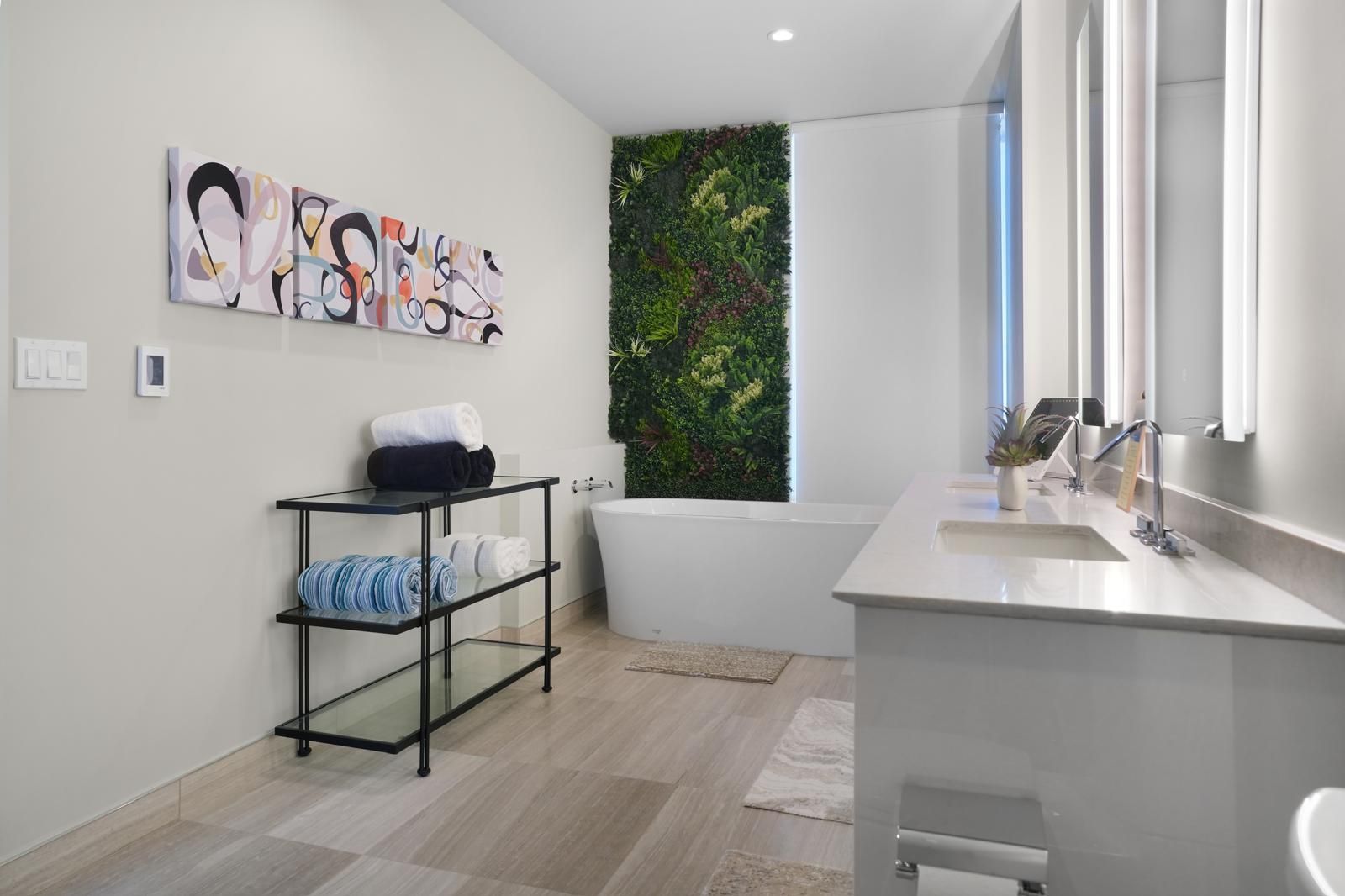 A bathroom with two sinks , a tub and a painting on the wall.