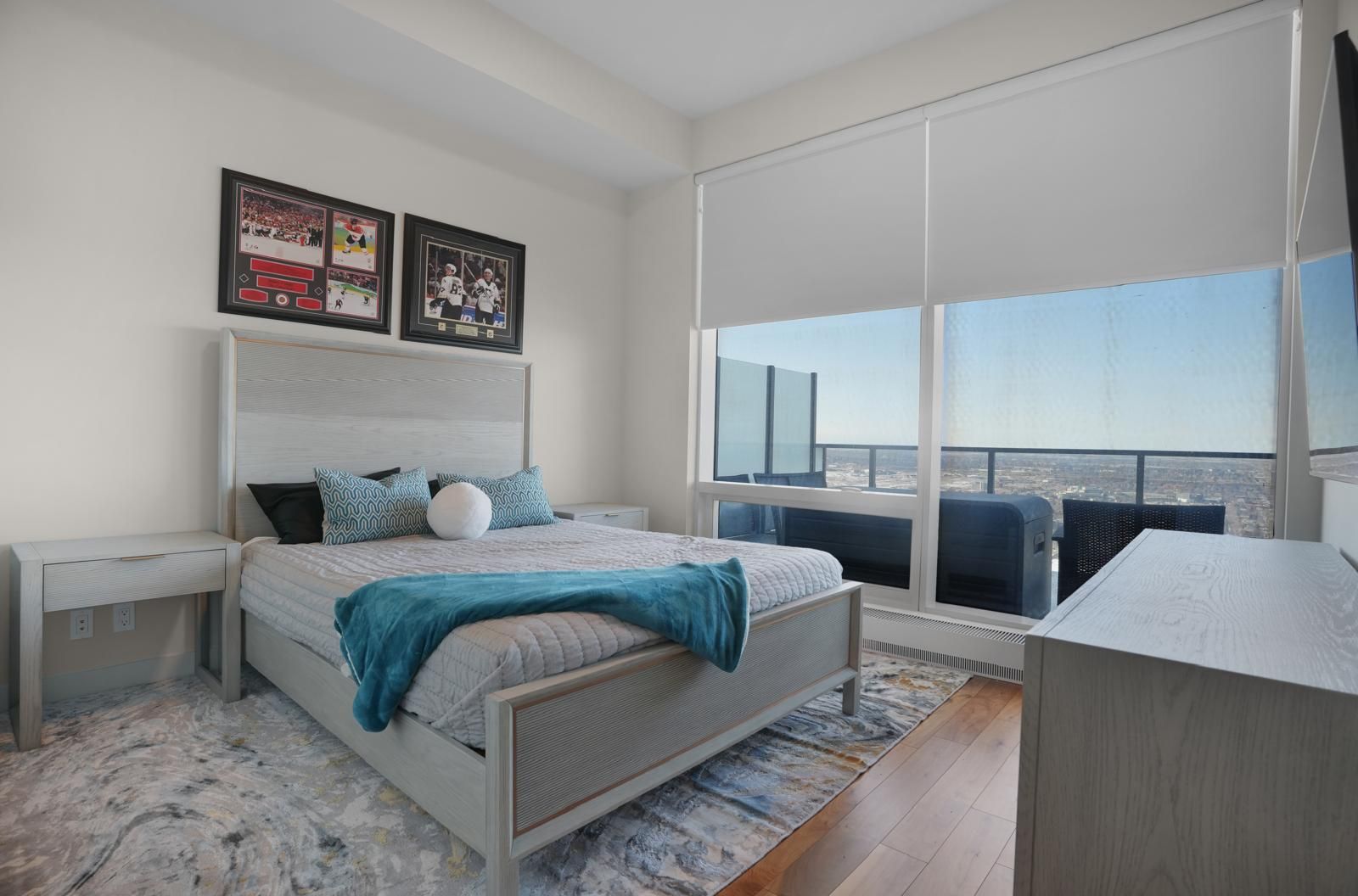 A bedroom with a king size bed , dresser , nightstand , and large windows.