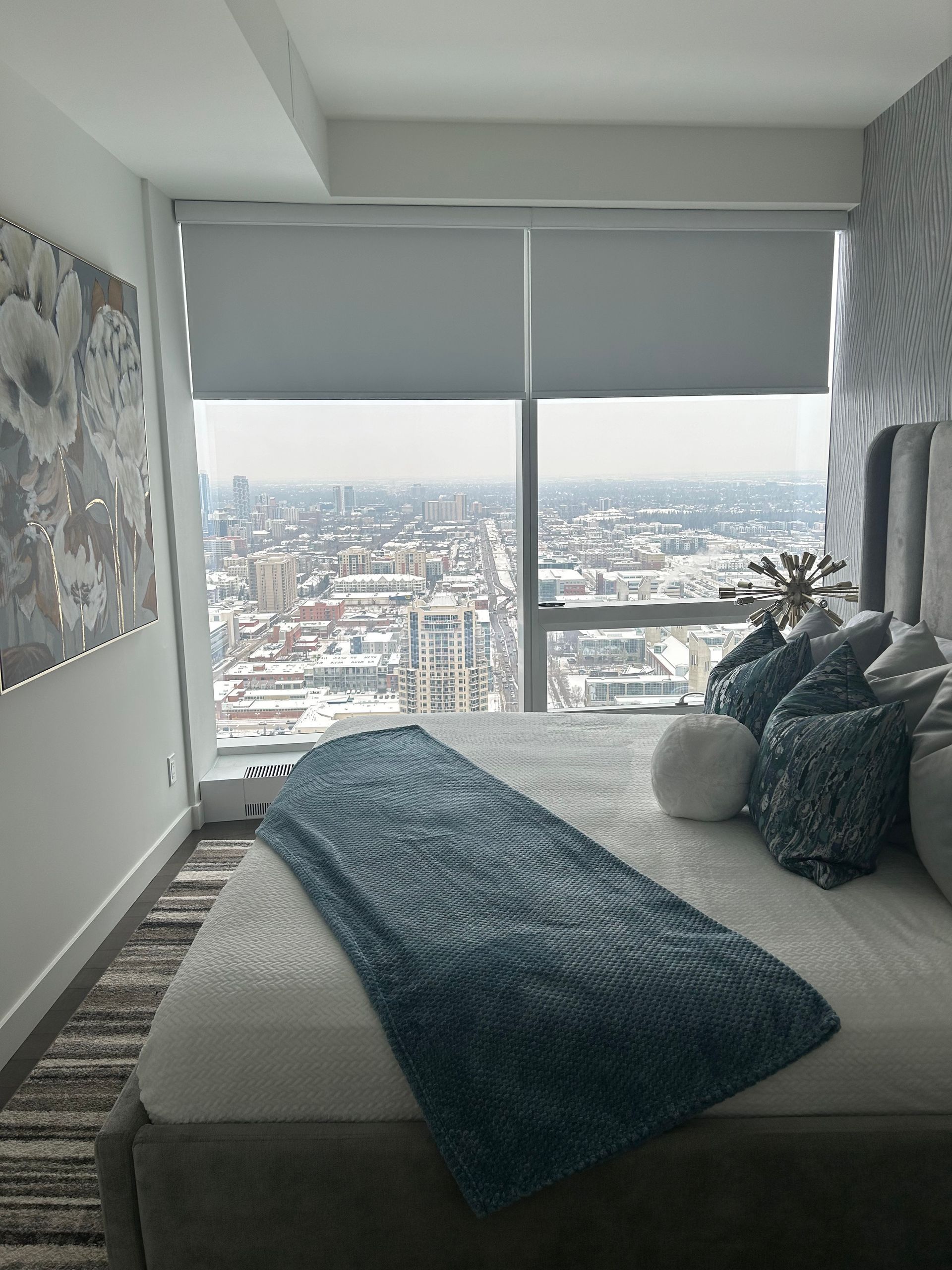 A bedroom with a large bed and a large window with a view of the city.