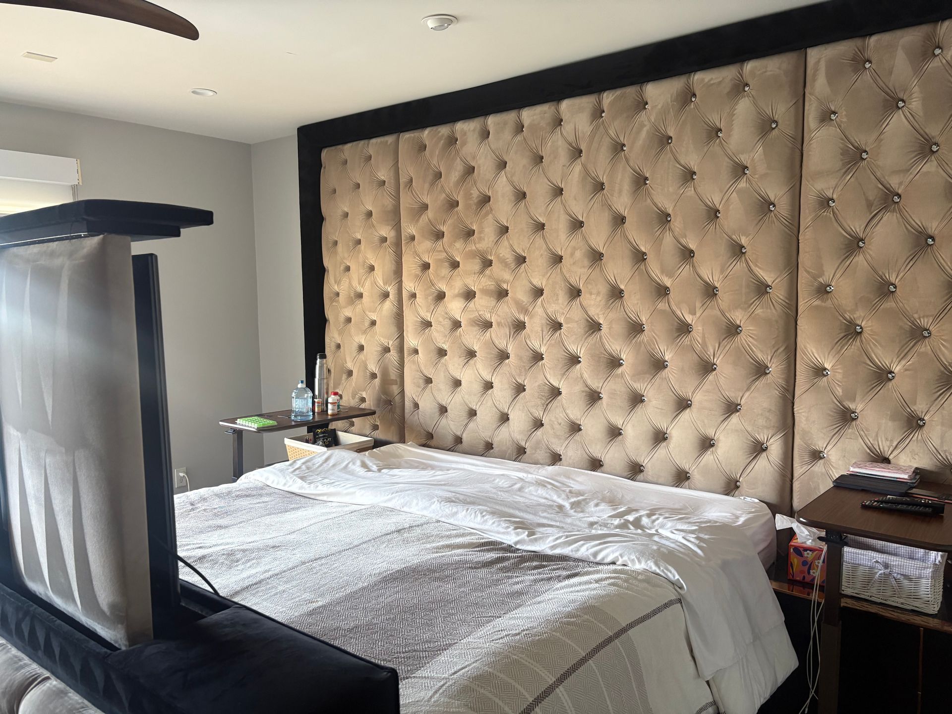 Beige tufted headboard, black bed frame, bed with white bedding, small table.