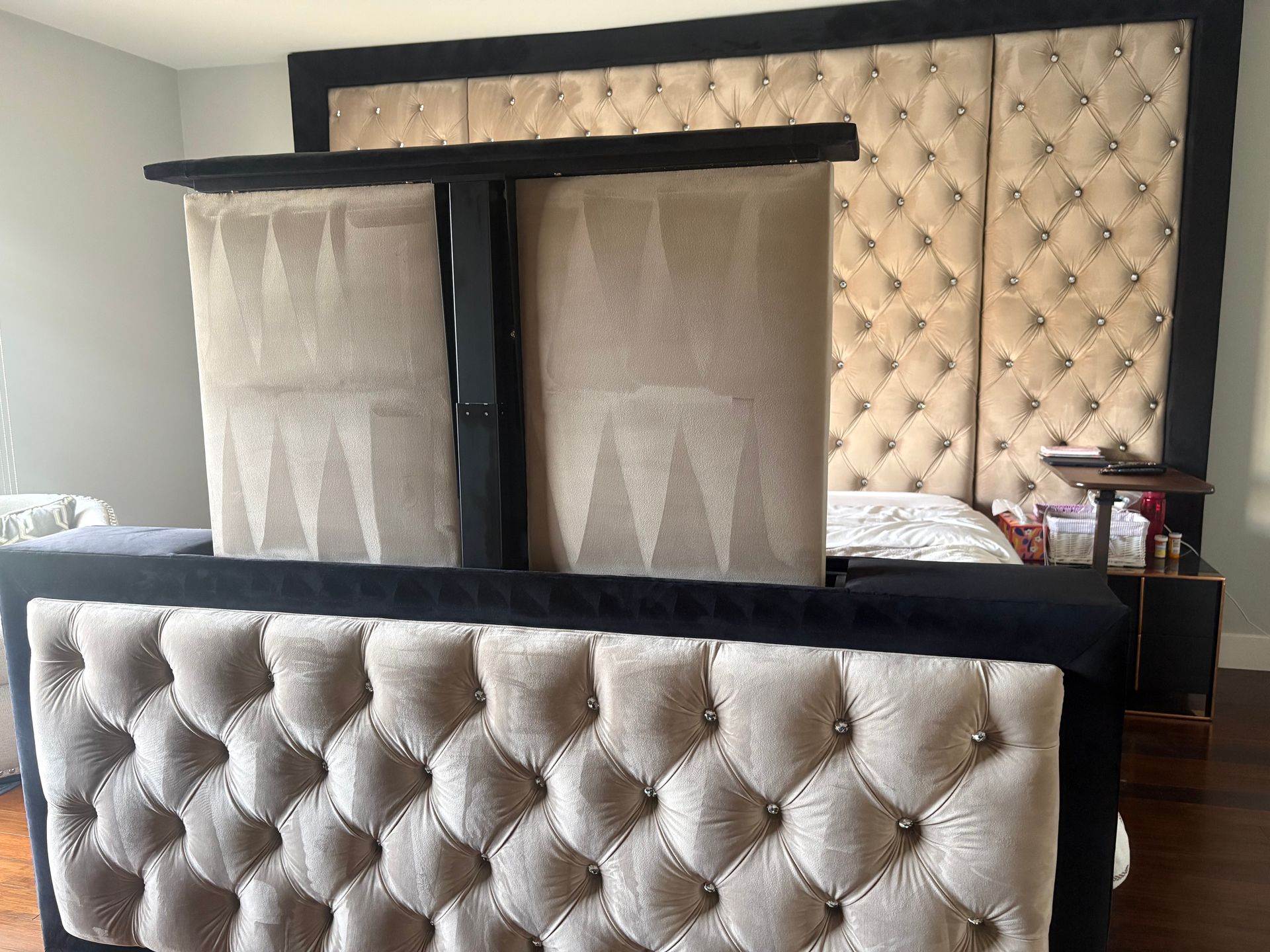 Tufted upholstered bed with TV lift, neutral tones, and black trim.