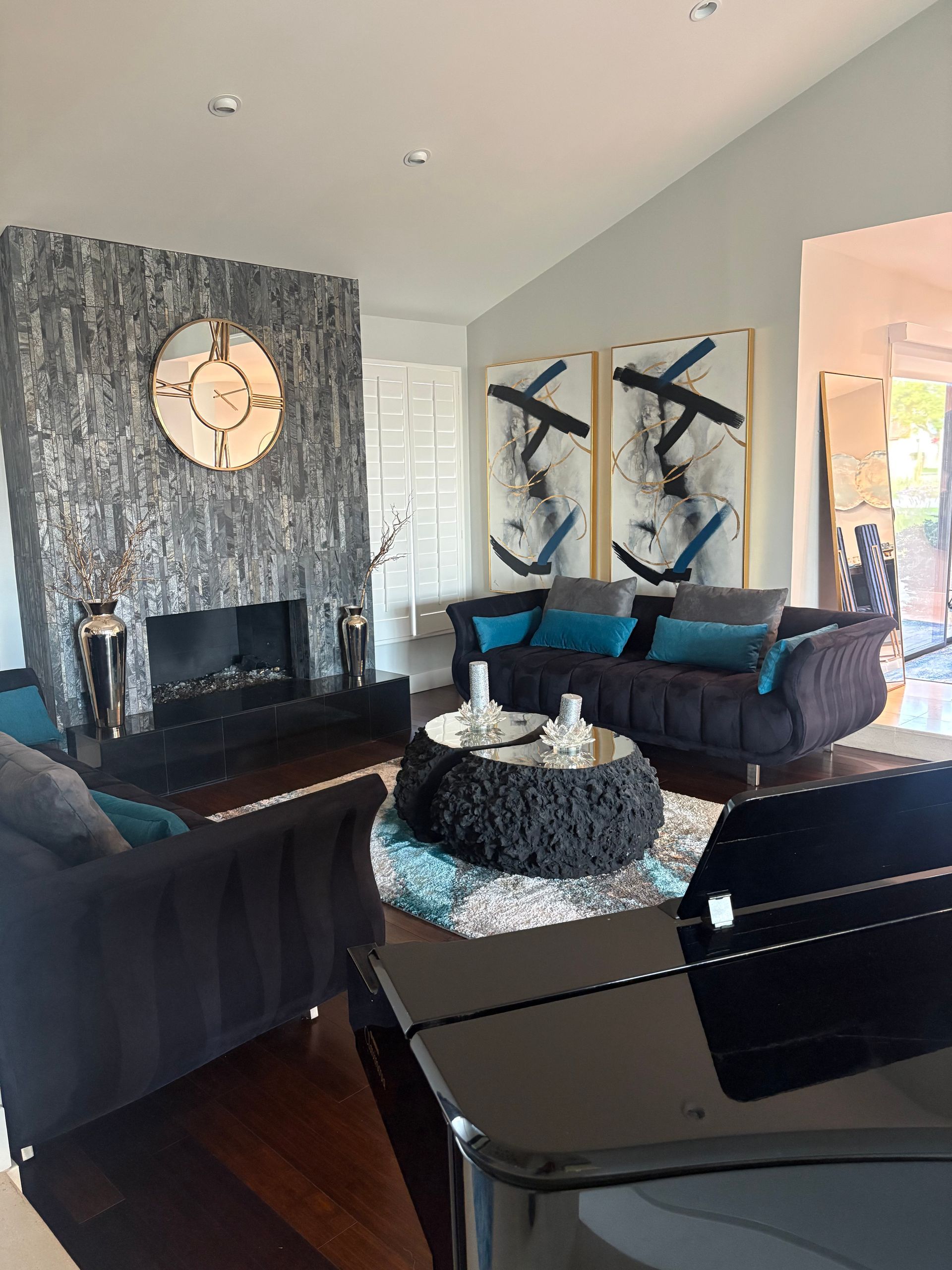 Living room with fireplace, sofa, art, and a piano. Gray, black, and turquoise color scheme.