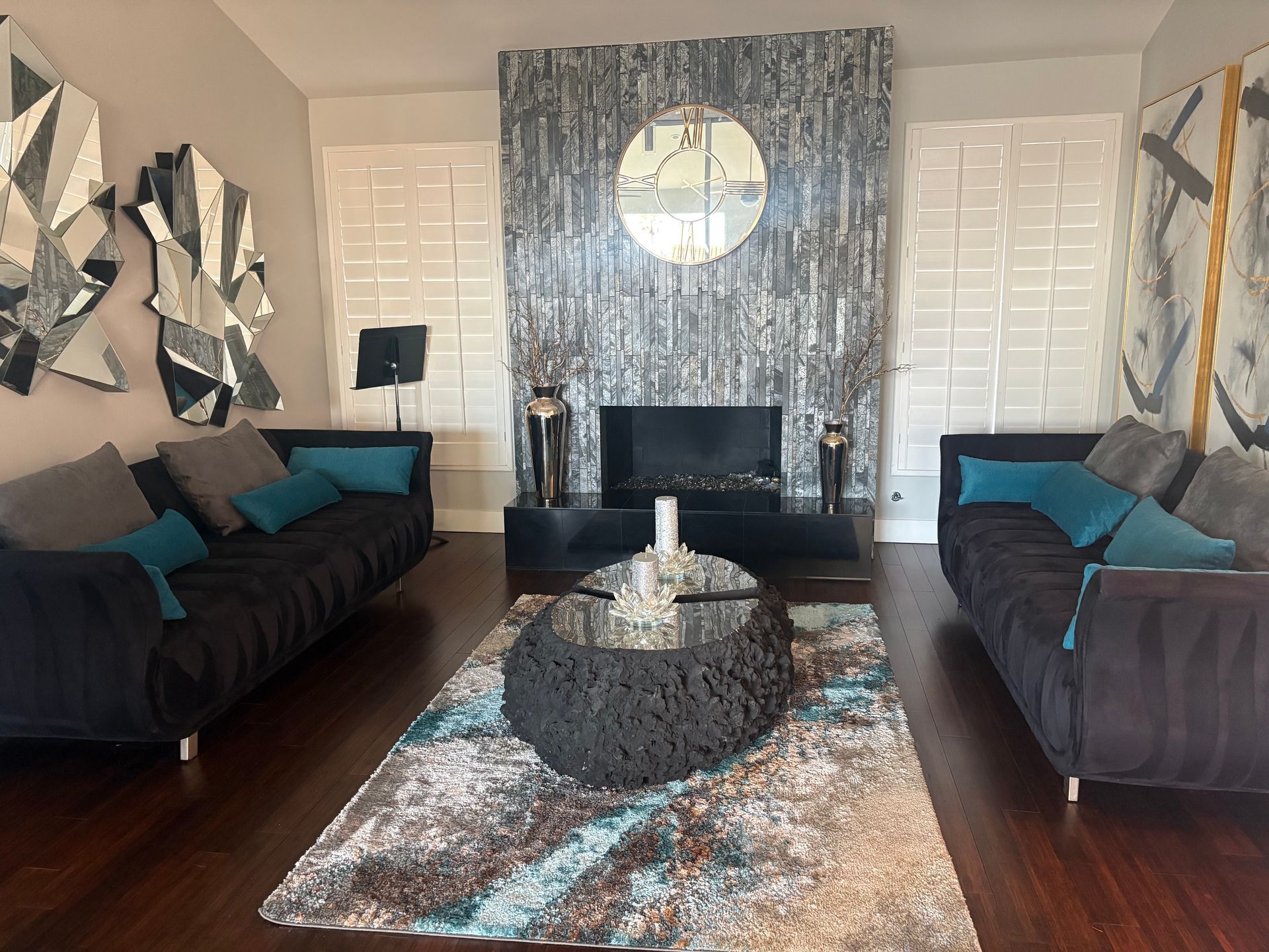 Living room with black sofas, teal pillows, a textured rug, and fireplace with a circular mirror.