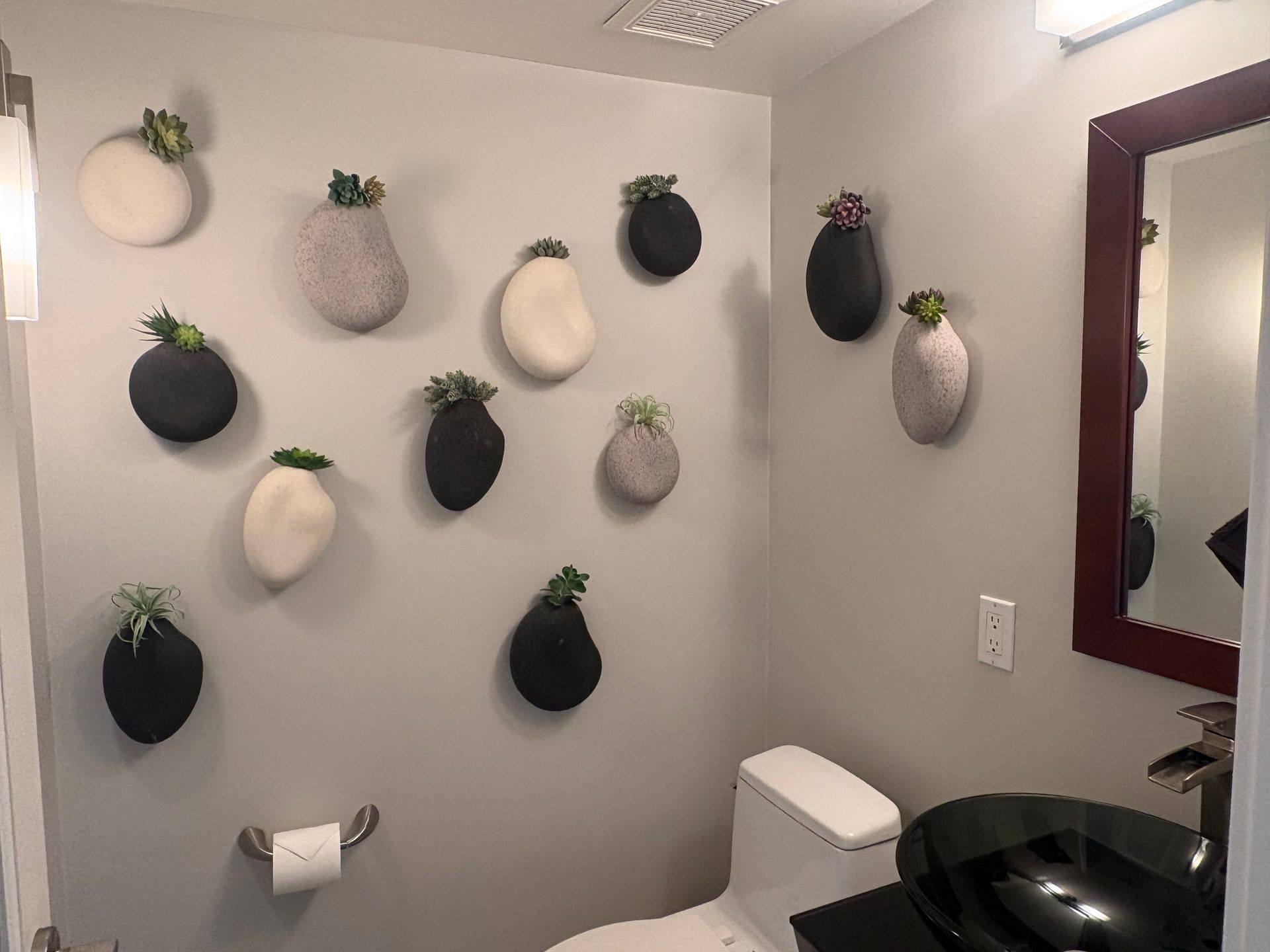 Bathroom with wall-mounted planters, toilet, dark-colored sink, and mirror. Gray walls and neutral tones.