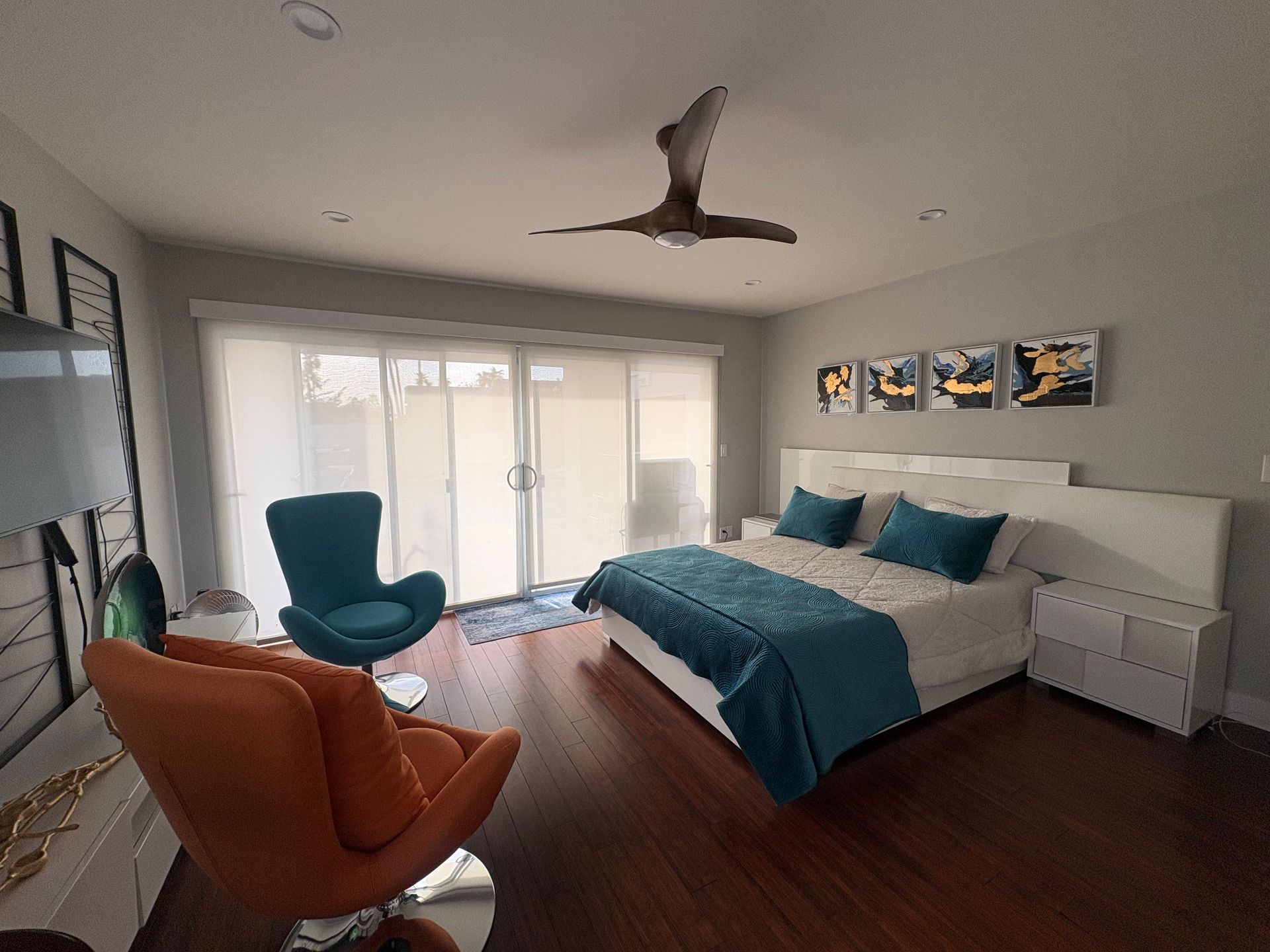 Bedroom with bed, teal throw, two armchairs, and sliding glass doors.