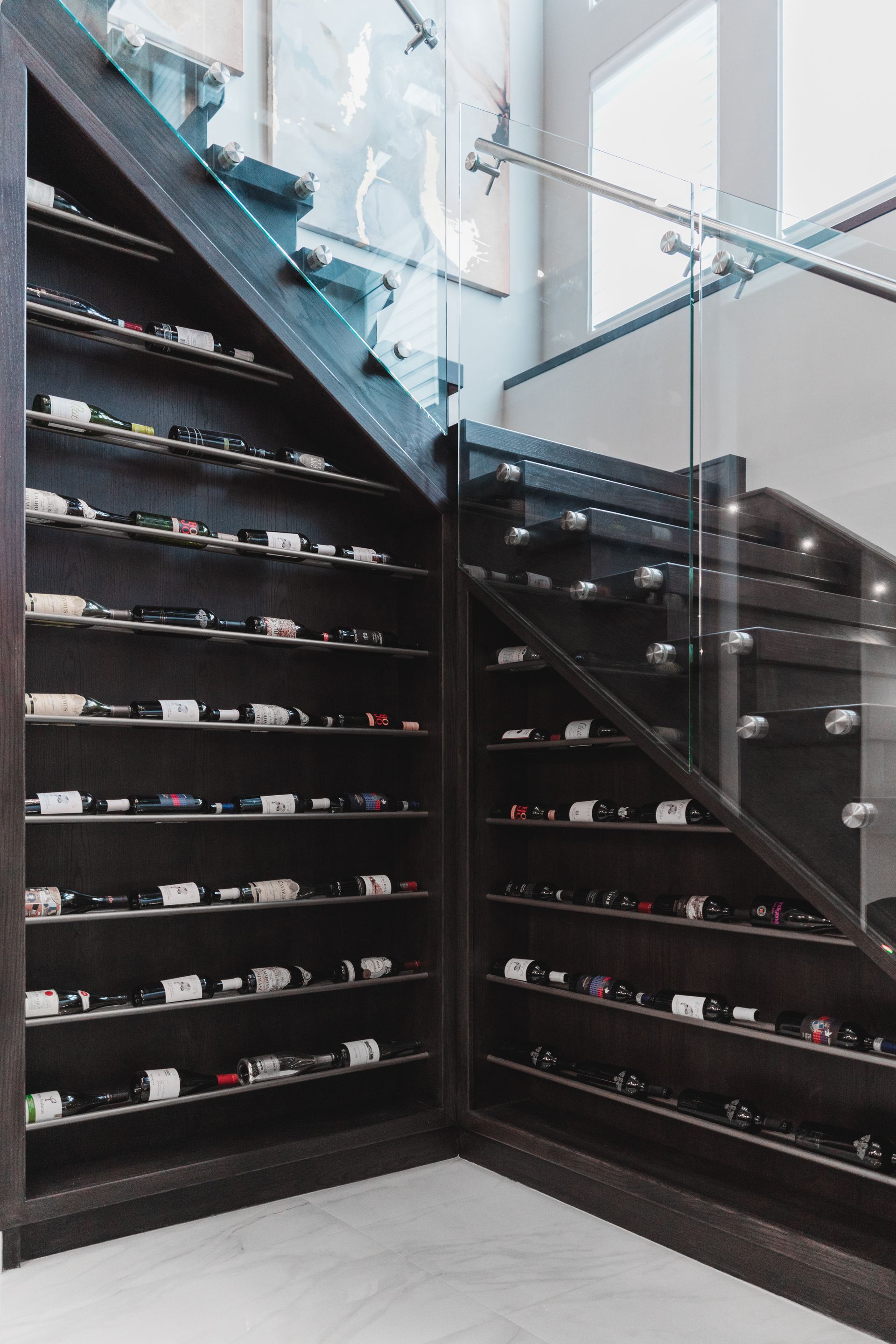 There are many bottles of wine on the shelves under the stairs.