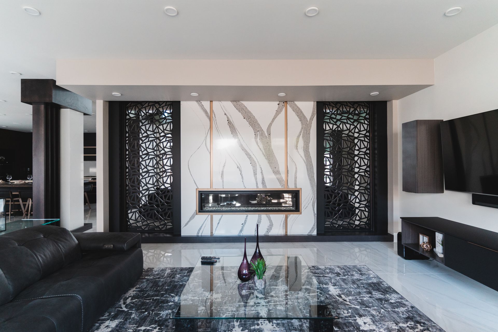 A living room with a black couch , a glass coffee table , and a fireplace.