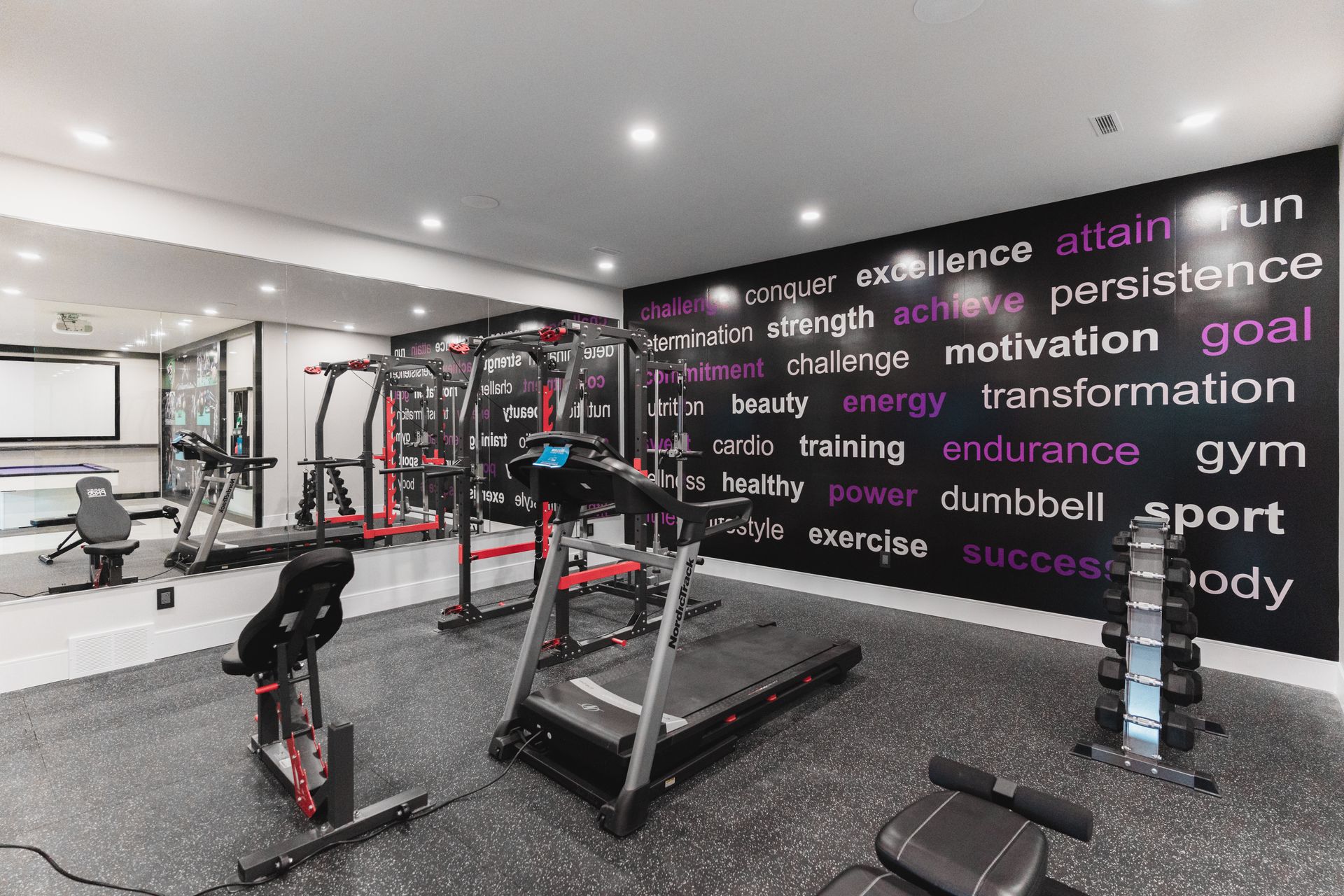 A gym with a treadmill , bike , dumbbells and a wall covered in words.