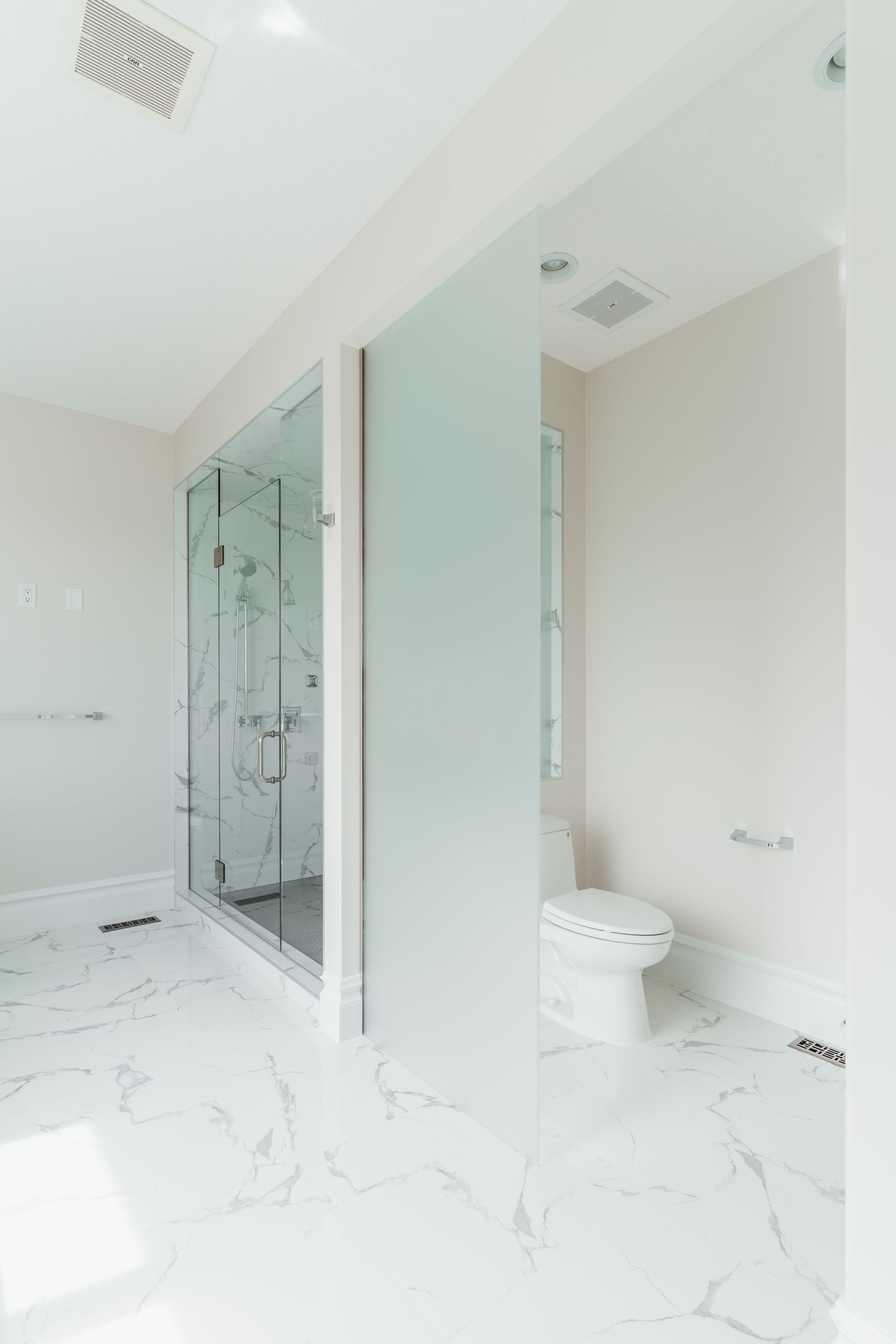 A bathroom with a toilet , shower , and glass door.