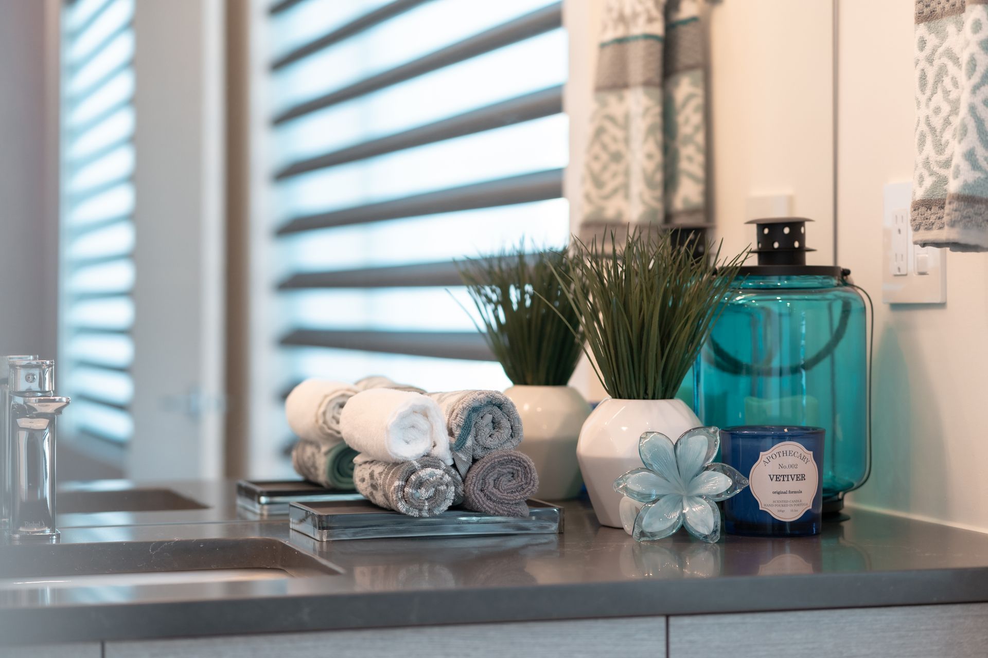 A bathroom counter with a sink , towels , candles , and potted plants.
