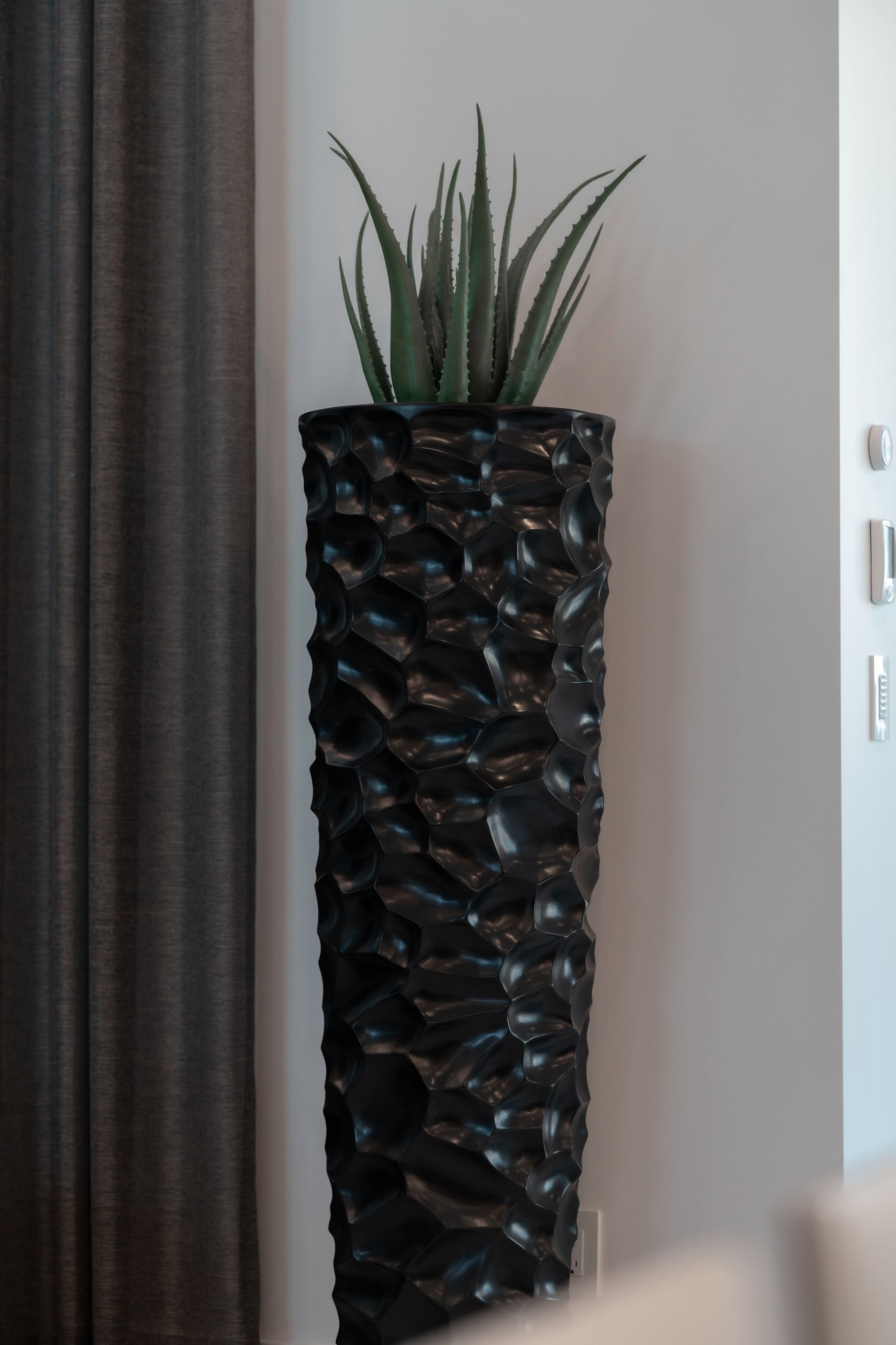 A tall black vase with a plant in it.