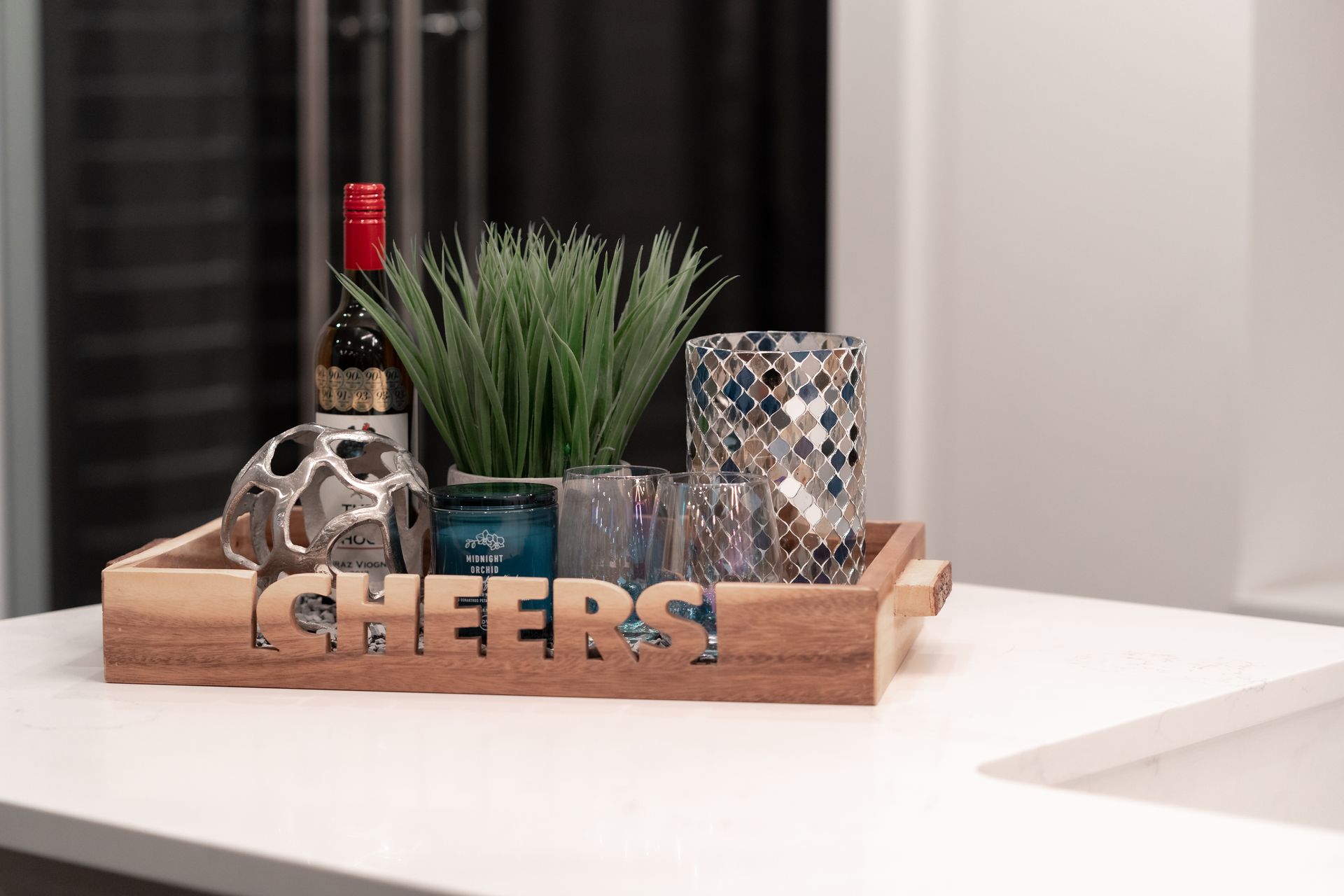 A wooden tray with a bottle of wine , glasses , and a plant on it.
