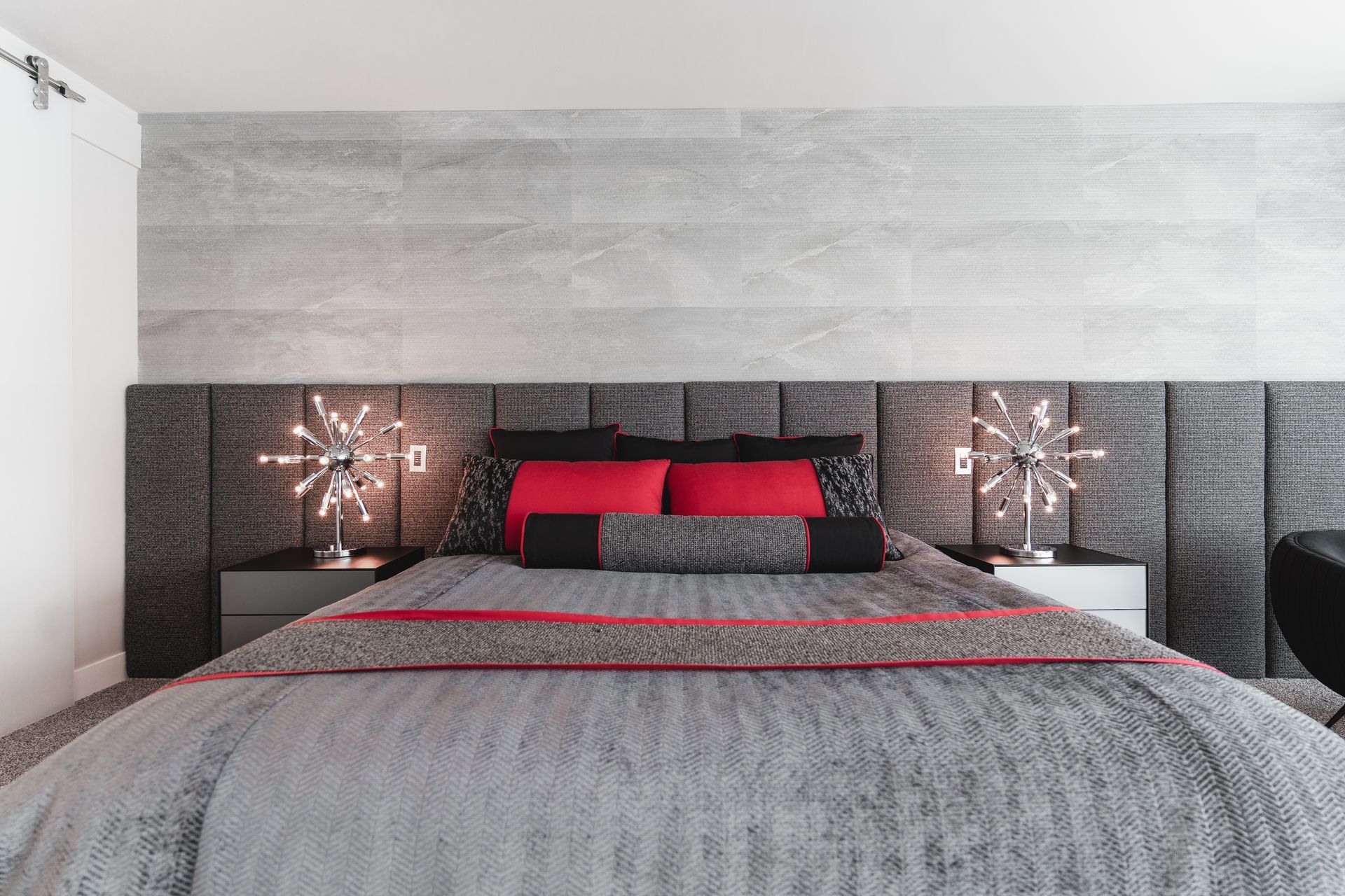A bedroom with a bed , nightstands , lamps and a gray wall.