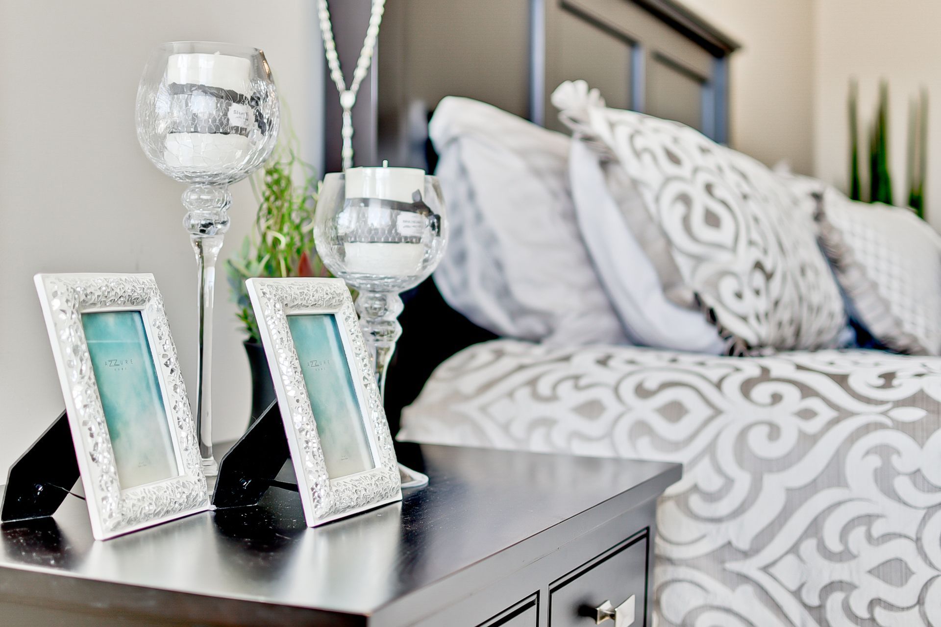 A bedroom with a bed , nightstand , picture frames and candles.