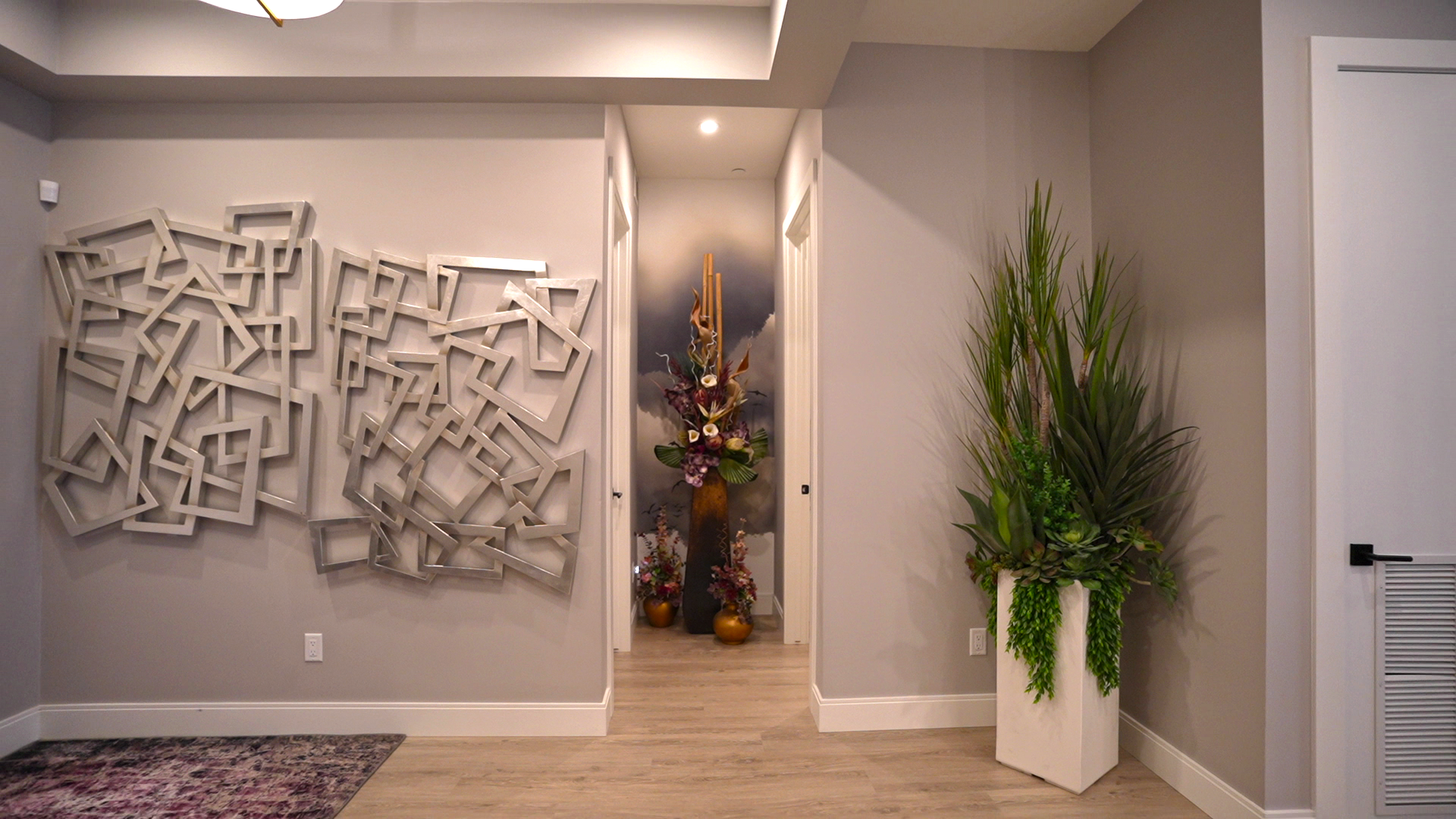 A hallway with a painting on the wall and a potted plant.