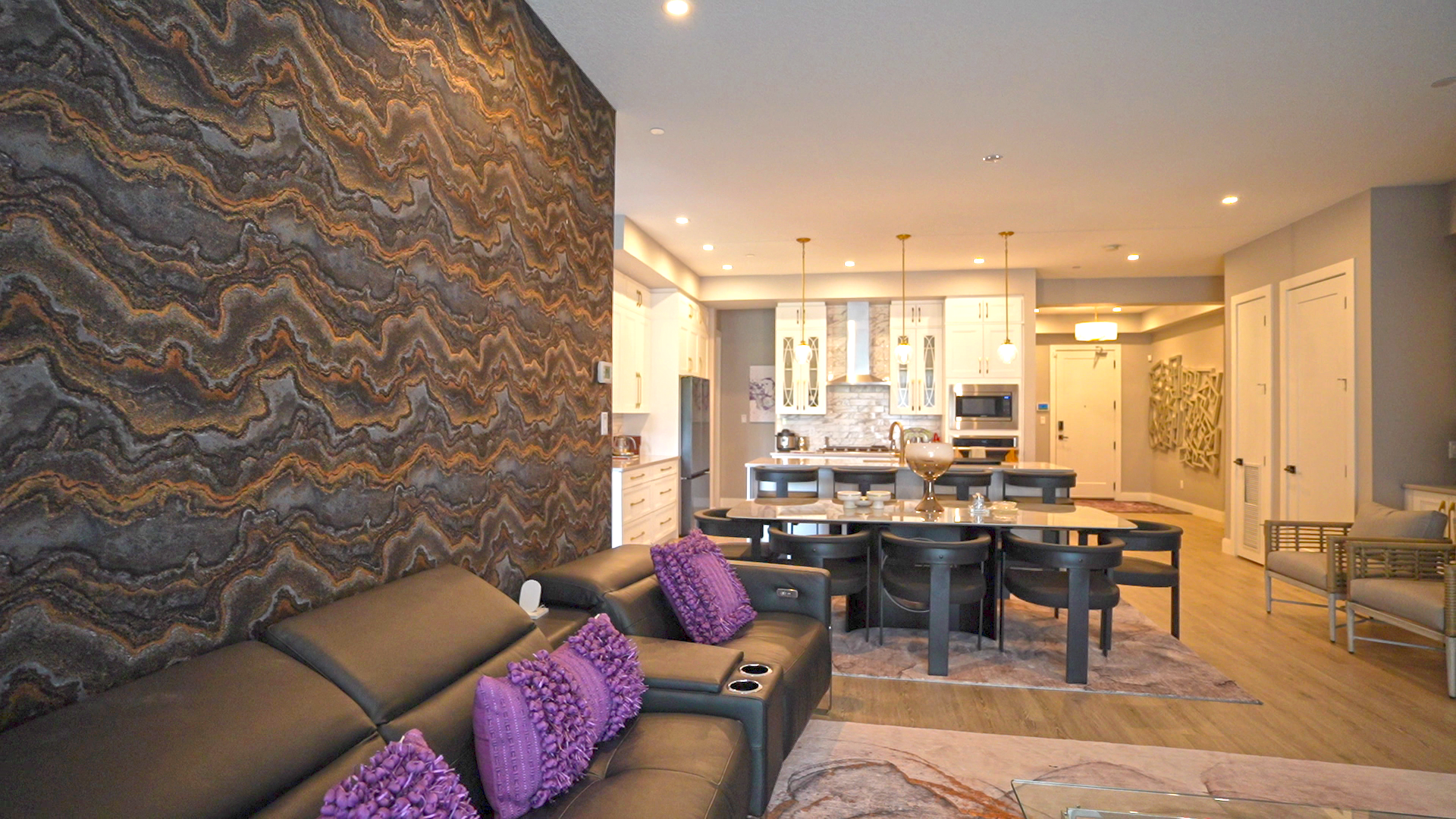 A living room with a black couch and purple pillows and a dining room with a table and chairs.
